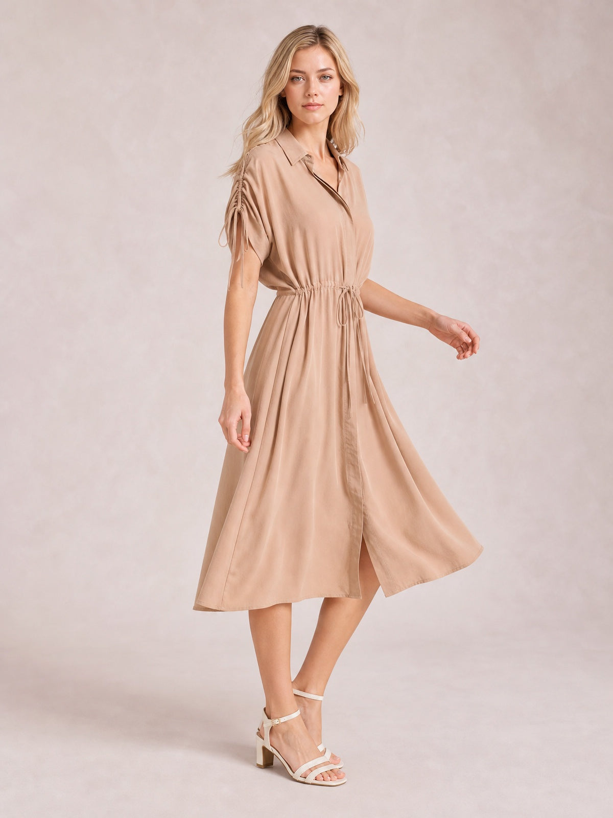 Model poses in a tan drawstring collared neck midi dress with short sleeves, buttoned front, gathered waist, and softly flared skirt.
