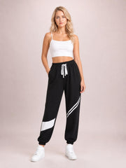 Model stands with one hand in a pocket wearing black contrast joggers with white drawstring, side stripes, pockets, and elasticized cuffs.