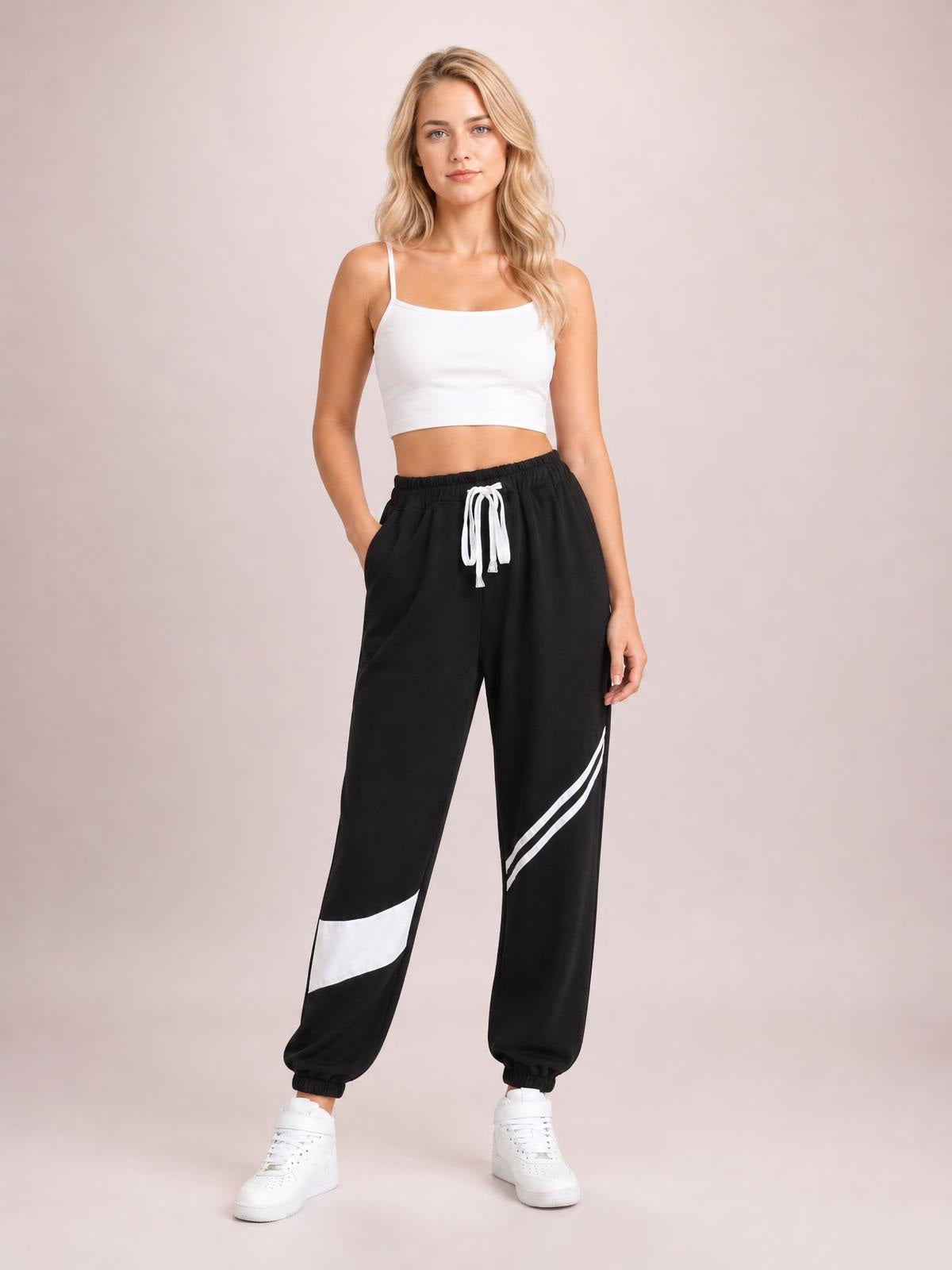 Model stands with one hand in a pocket wearing black contrast joggers with white drawstring, side stripes, pockets, and elasticized cuffs.