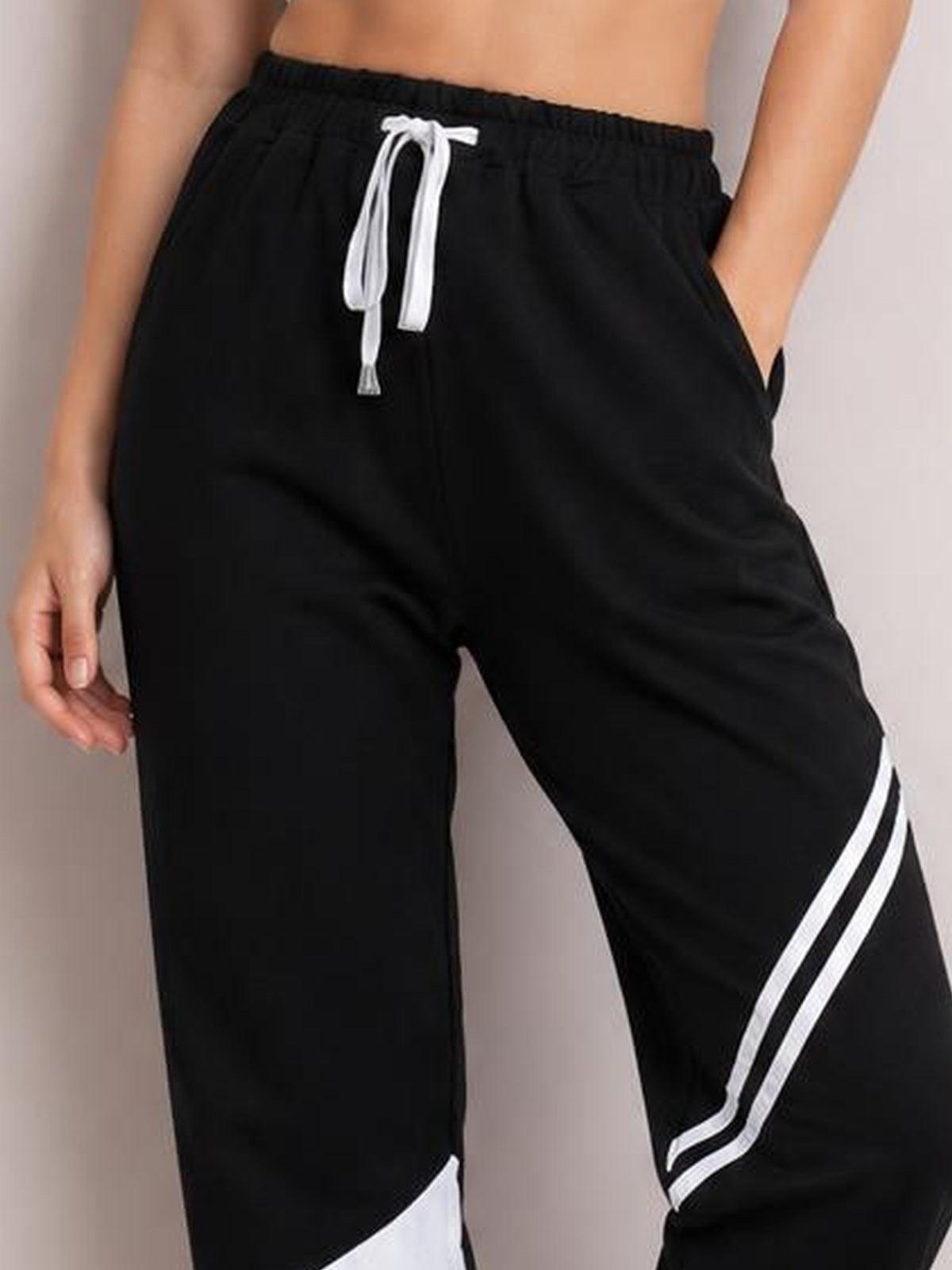 Model wears black contrast joggers with a white drawstring, side pockets, and bold white leg stripes in a relaxed silhouette, posing with one hand in a pocket.