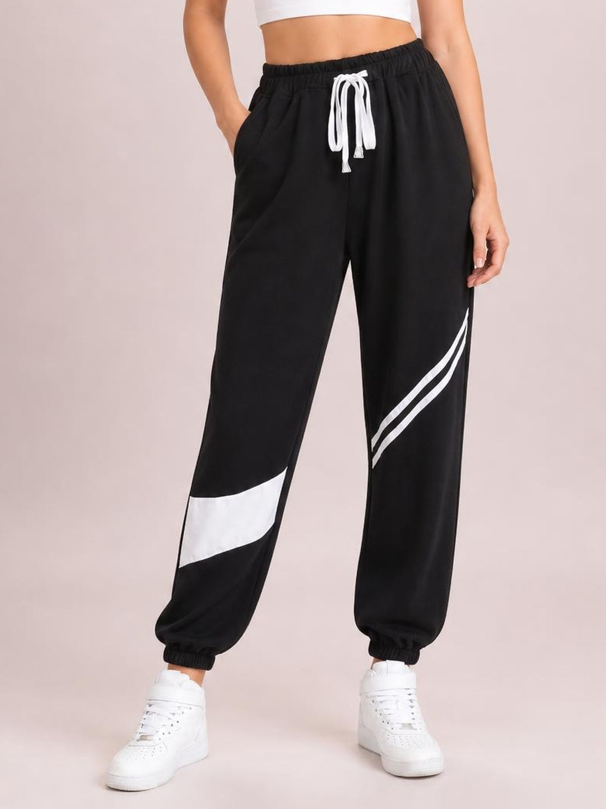 Model wearing black contrast joggers with a white drawstring, side pockets, bold white leg accents, relaxed fit, and elastic ankle cuffs.