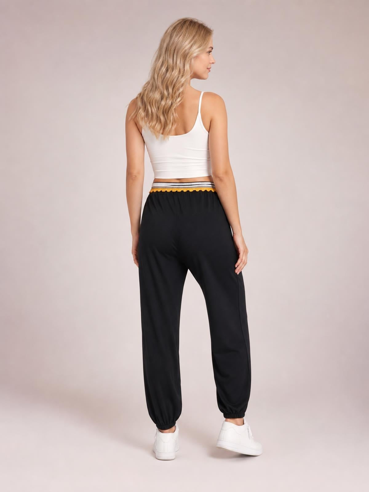 A model poses from the back in black contrast joggers with a striped waistband, relaxed tapered legs, and elastic ankle cuffs.