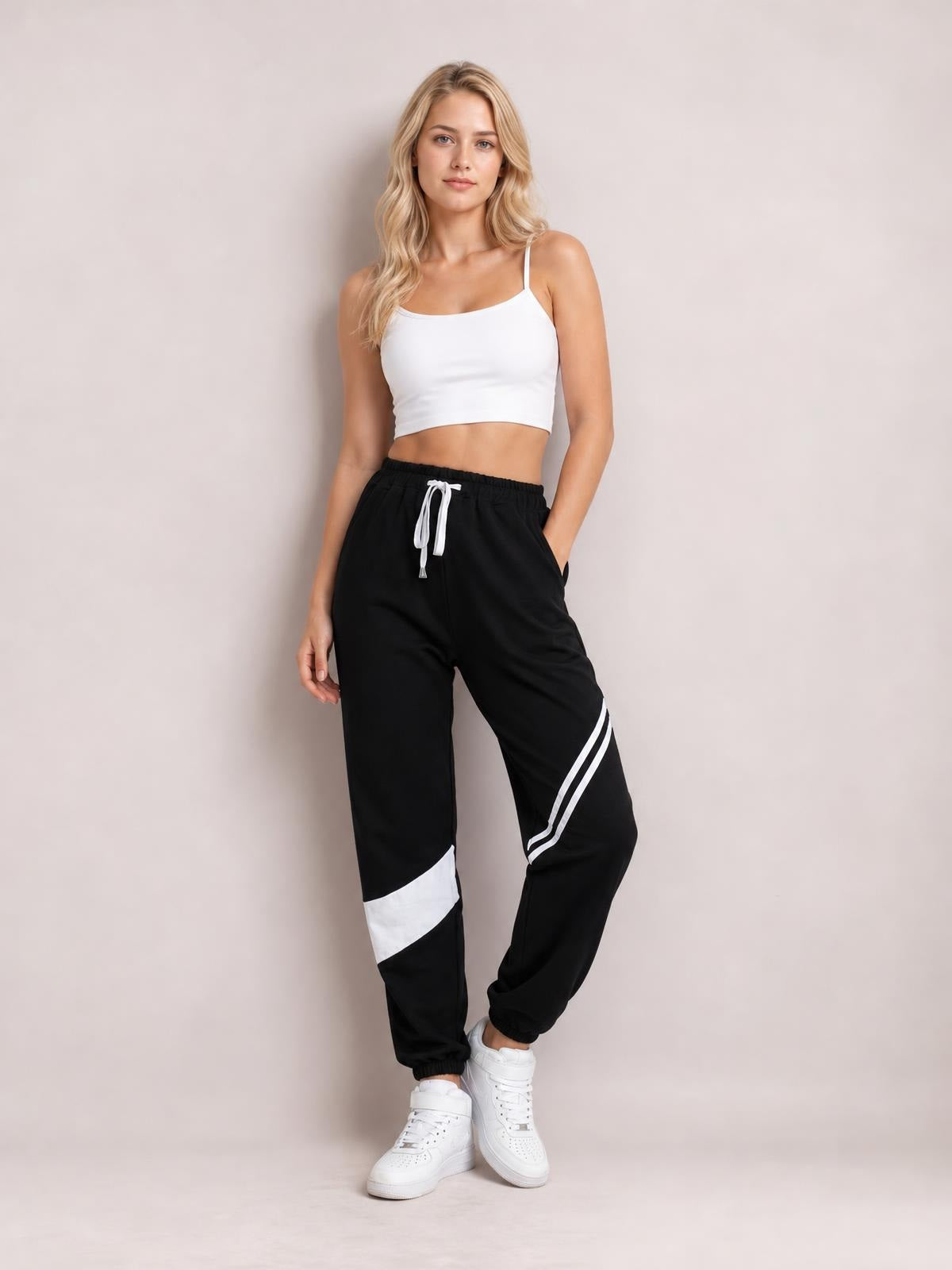 A model poses in black drawstring contrast joggers with white stripe and panel accents, side pockets, a relaxed fit, and tapered elastic cuffs.