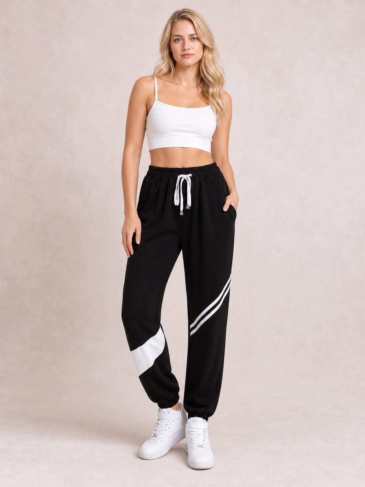 A model stands in black contrast joggers with a white drawstring, side pockets, striped leg panels, elastic cuffs, and a relaxed tapered silhouette.