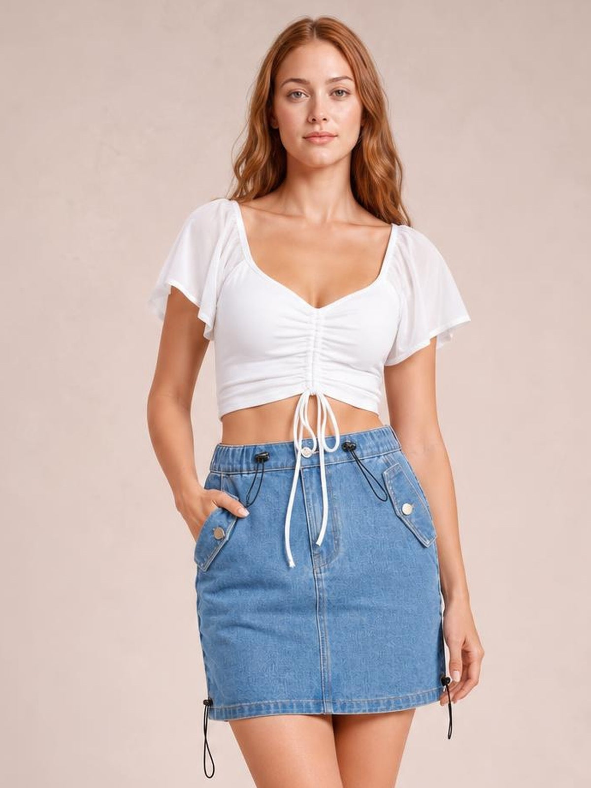 Model poses in a blue denim skirt with a drawstring waist, buttoned front, flap pockets, and a straight above-the-knee silhouette.