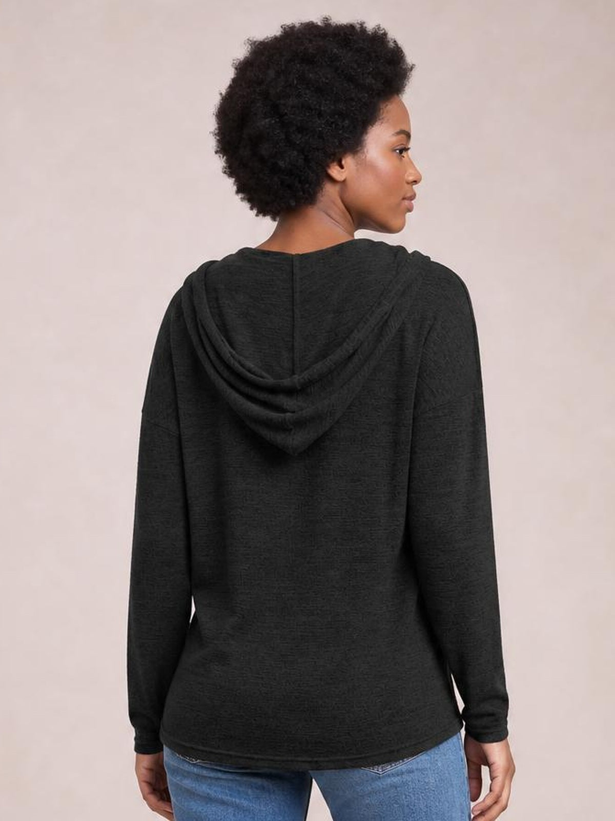 A model looks over her shoulder wearing a black hooded T-shirt with dropped shoulders, long sleeves, and a relaxed straight silhouette.