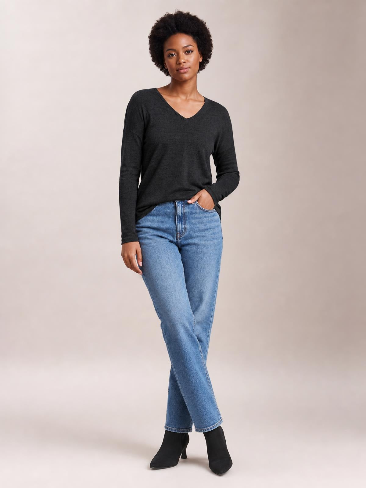 Model poses in a dark charcoal long-sleeve T-shirt with a V-neck, relaxed straight silhouette, and slightly draped construction.