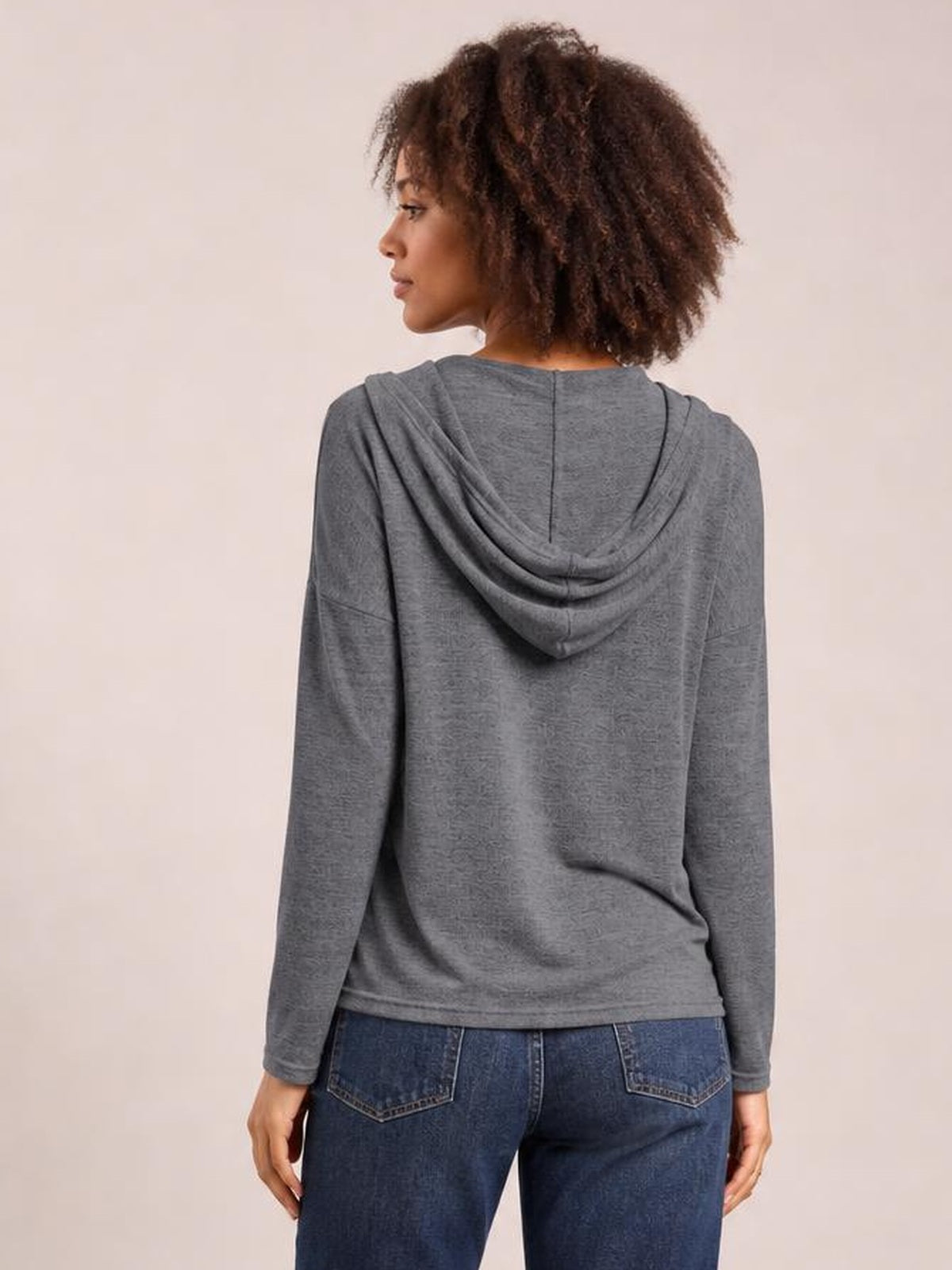 A model faces away in a relaxed gray hooded T-shirt with dropped shoulders, long sleeves, a draped hood, and a straight silhouette.