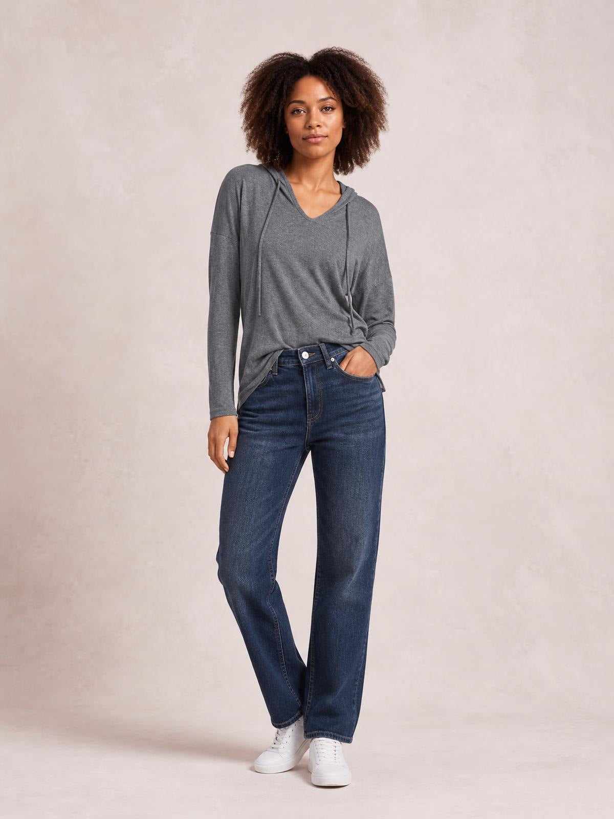 Model wears a gray drawstring dropped-shoulder hooded T-shirt with long sleeves and a relaxed silhouette, posing with one hand in her jeans pocket.