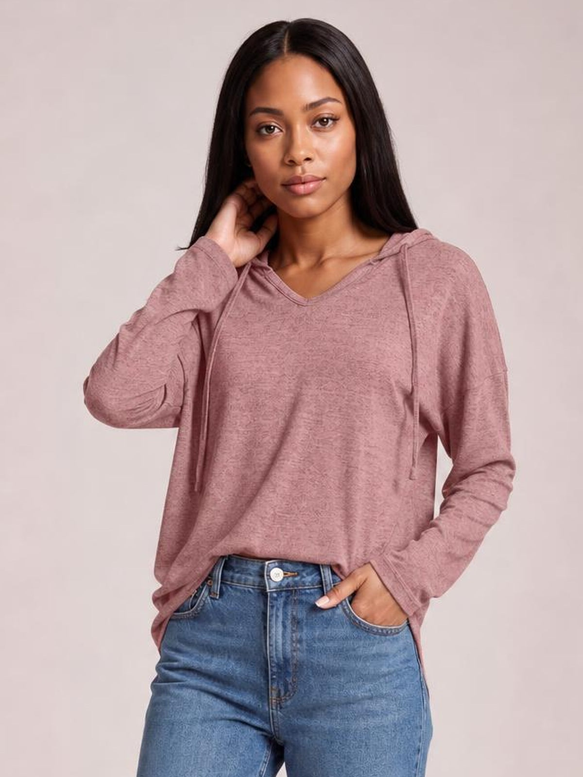 A model poses in a dusty rose drawstring hooded T-shirt with dropped shoulders, long sleeves, a relaxed loose silhouette, and subtle V-neck construction.