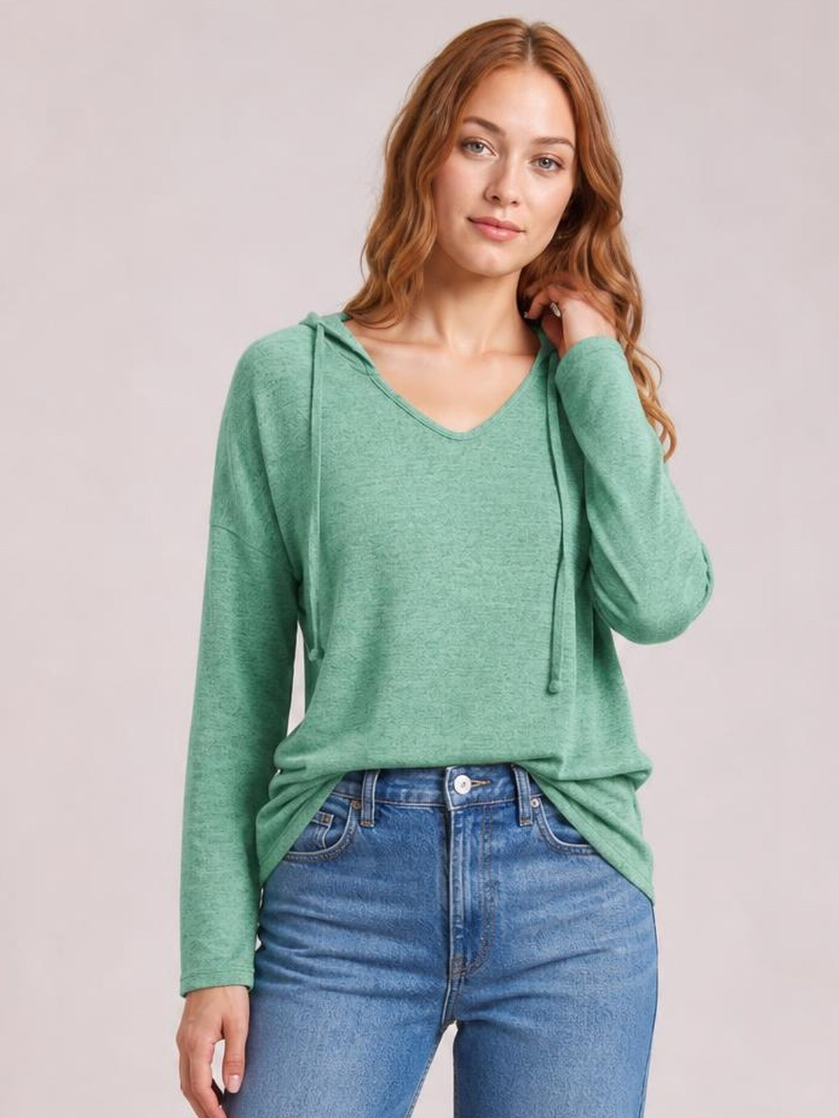 Model wears a relaxed mint green hooded T-shirt with dropped shoulders, long sleeves, V-neckline, and adjustable drawstrings, posing with one hand near her hair.