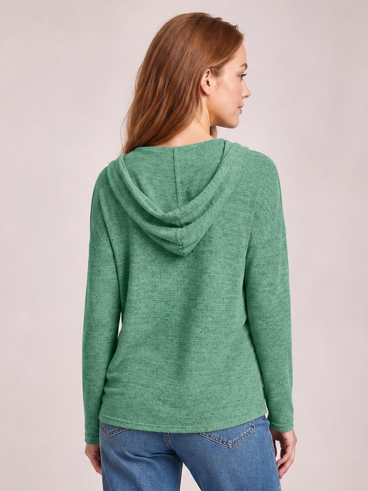 A model shown from the back wears a relaxed green hooded T-shirt with dropped shoulders, long sleeves, and a straight, easy-fitting silhouette.