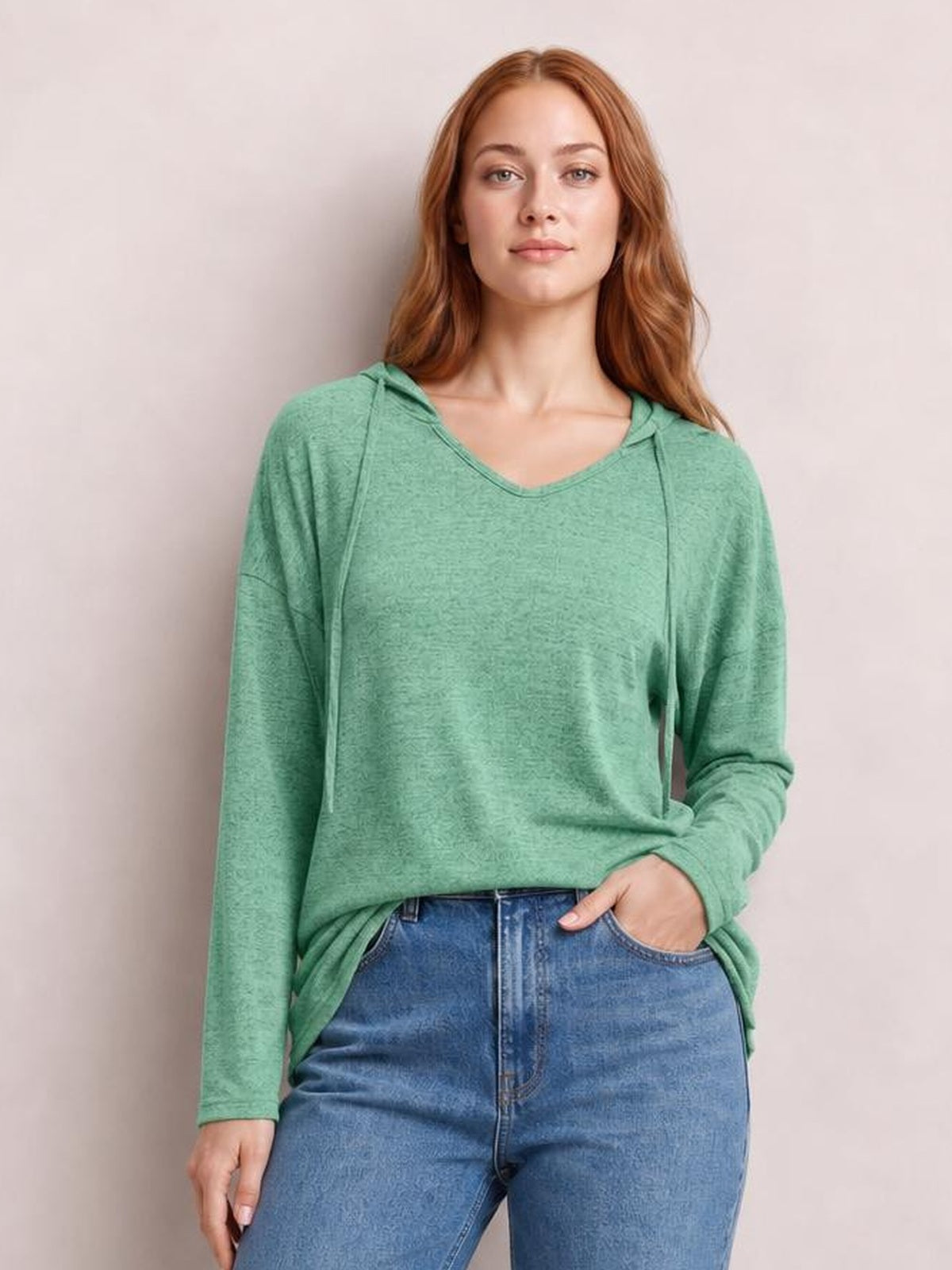Model wears a sage green drawstring dropped-shoulder hooded T-shirt with long sleeves and a relaxed silhouette, standing with one hand in her jeans pocket.