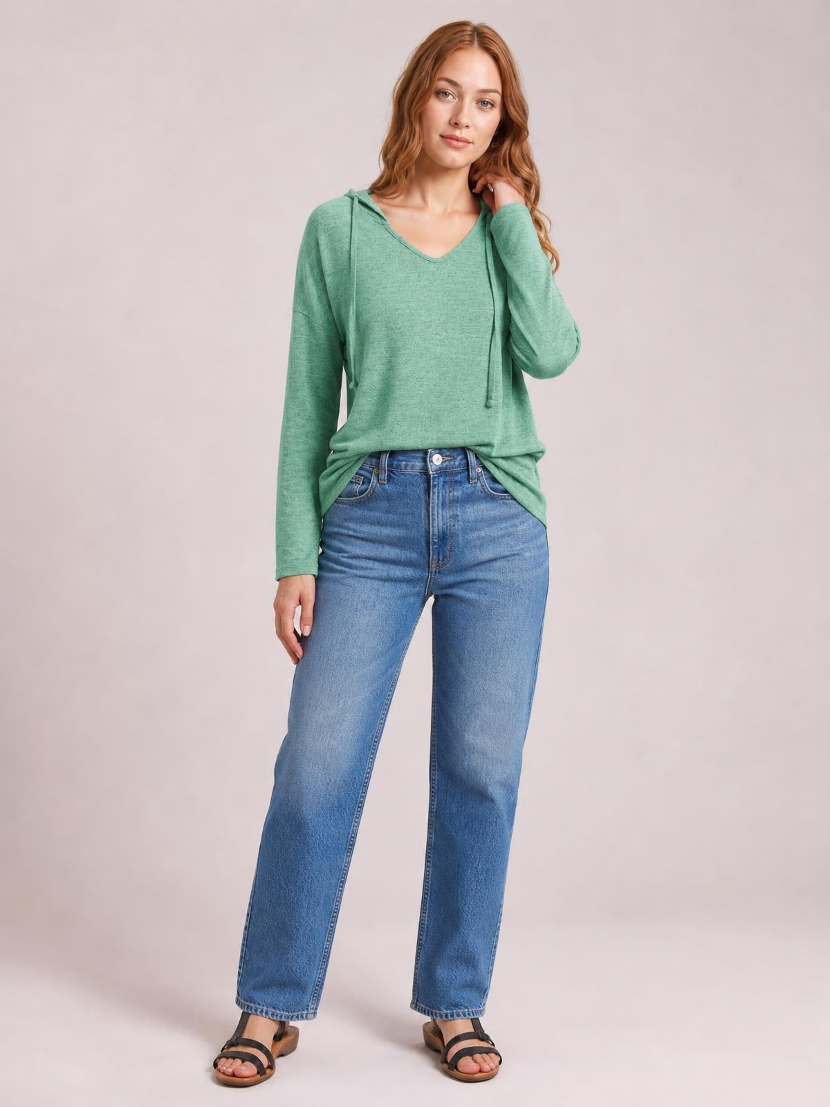 Model wears a relaxed green drawstring hooded T-shirt with dropped shoulders, long sleeves, V-neck, and an easy straight silhouette, touching her hair.