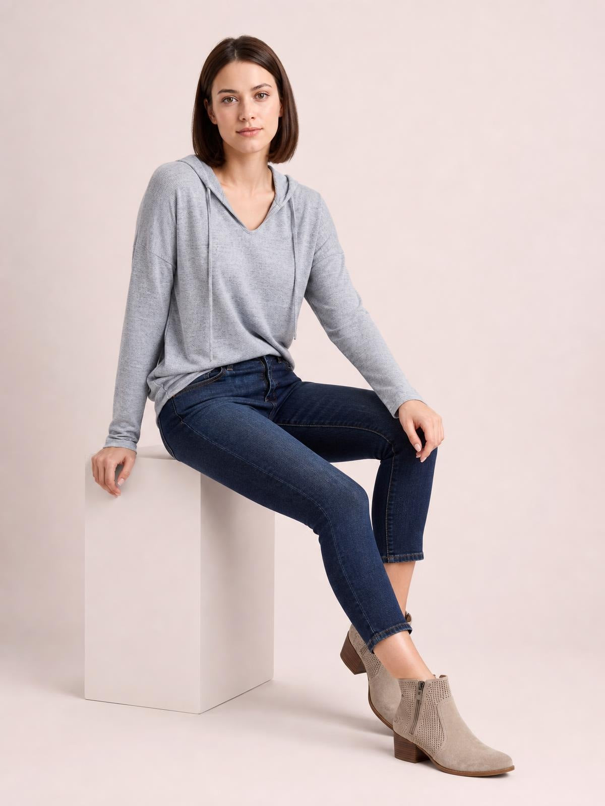 A seated model wears a light gray drawstring hooded T-shirt with dropped shoulders, long sleeves, a relaxed silhouette, and a softly draped construction.