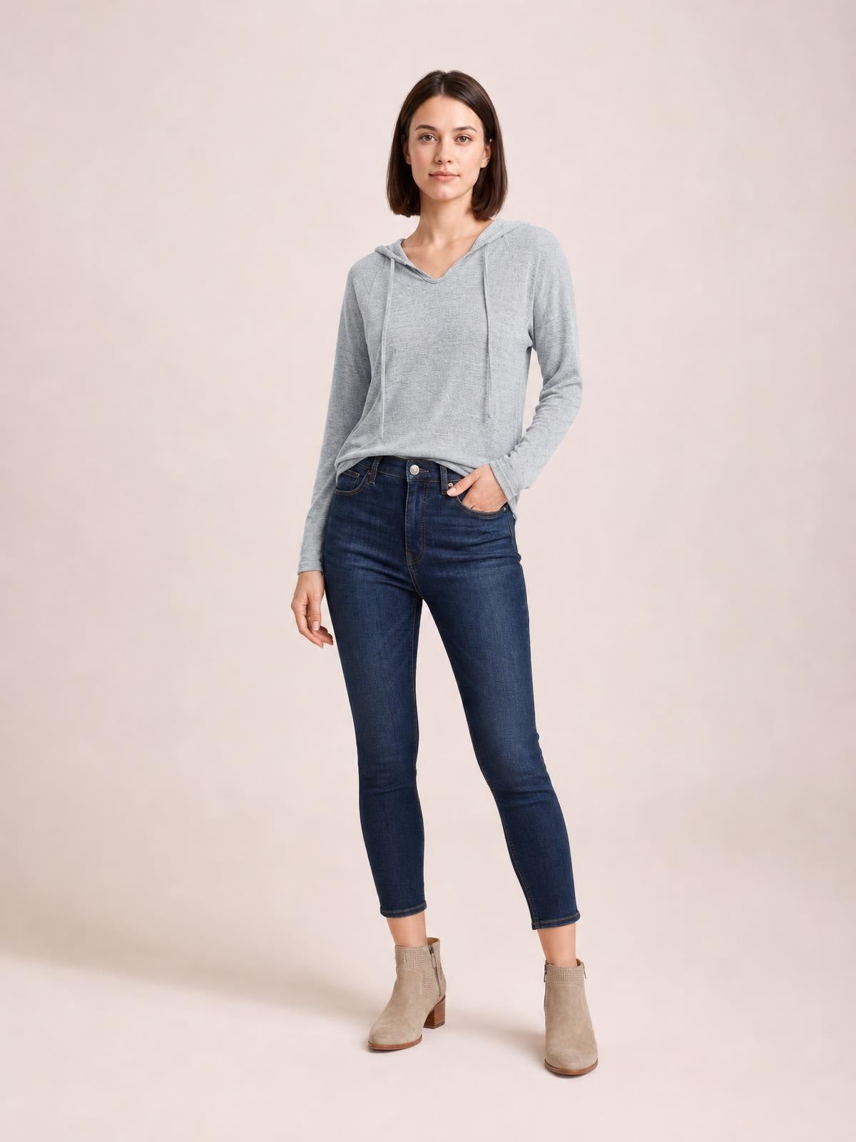 A model stands in a relaxed pose wearing a light gray drawstring hooded T-shirt with dropped shoulders, long sleeves, and an easy, slightly loose silhouette.