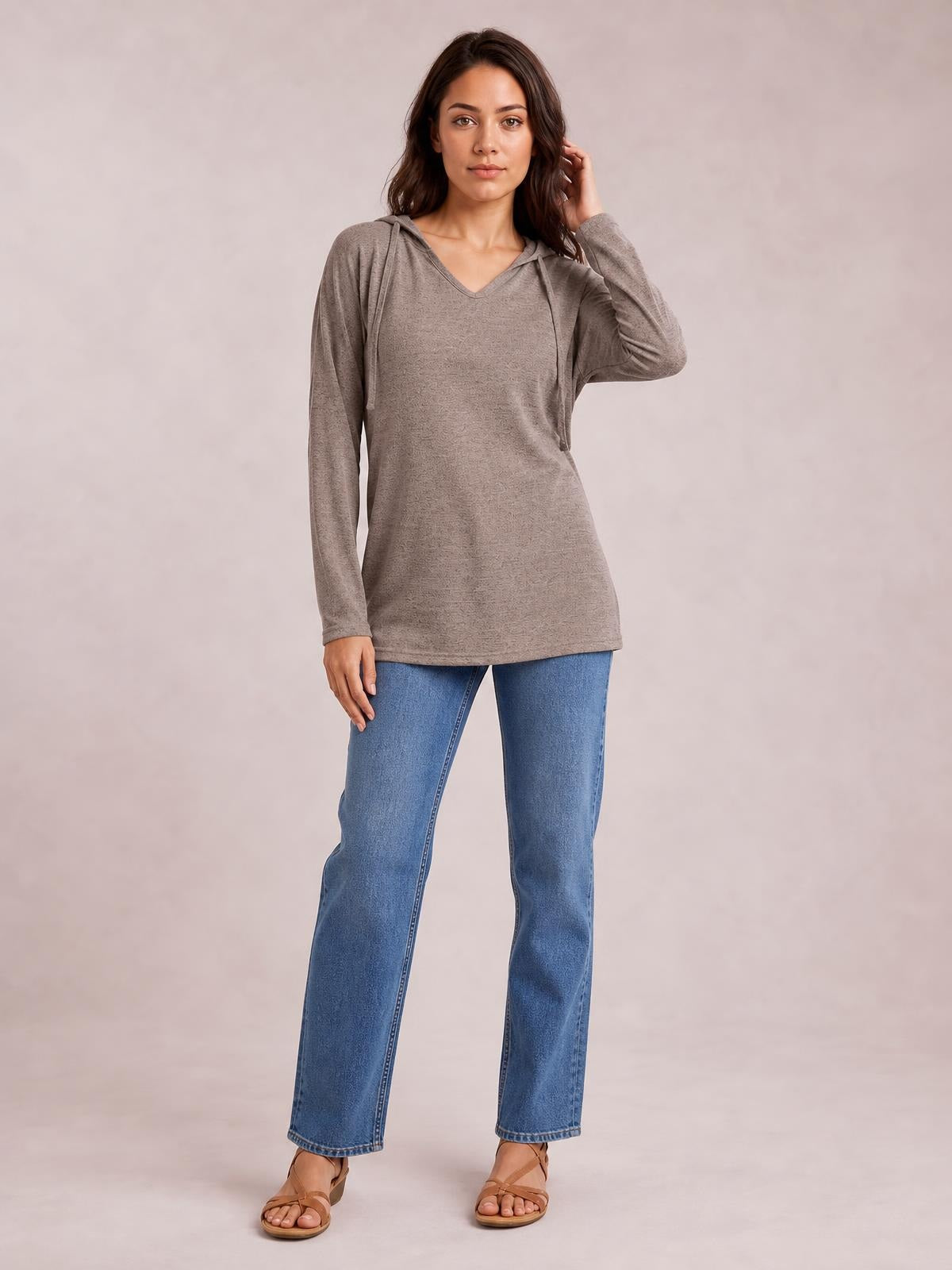 A woman models a taupe drawstring hooded T-shirt with dropped shoulders, long sleeves, a V-neck, and a relaxed tunic-length silhouette.