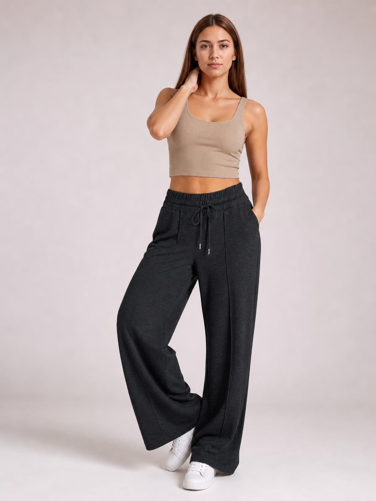 Model poses in dark gray drawstring elastic waist wide-leg pants with visible pockets and a relaxed, flowing silhouette.