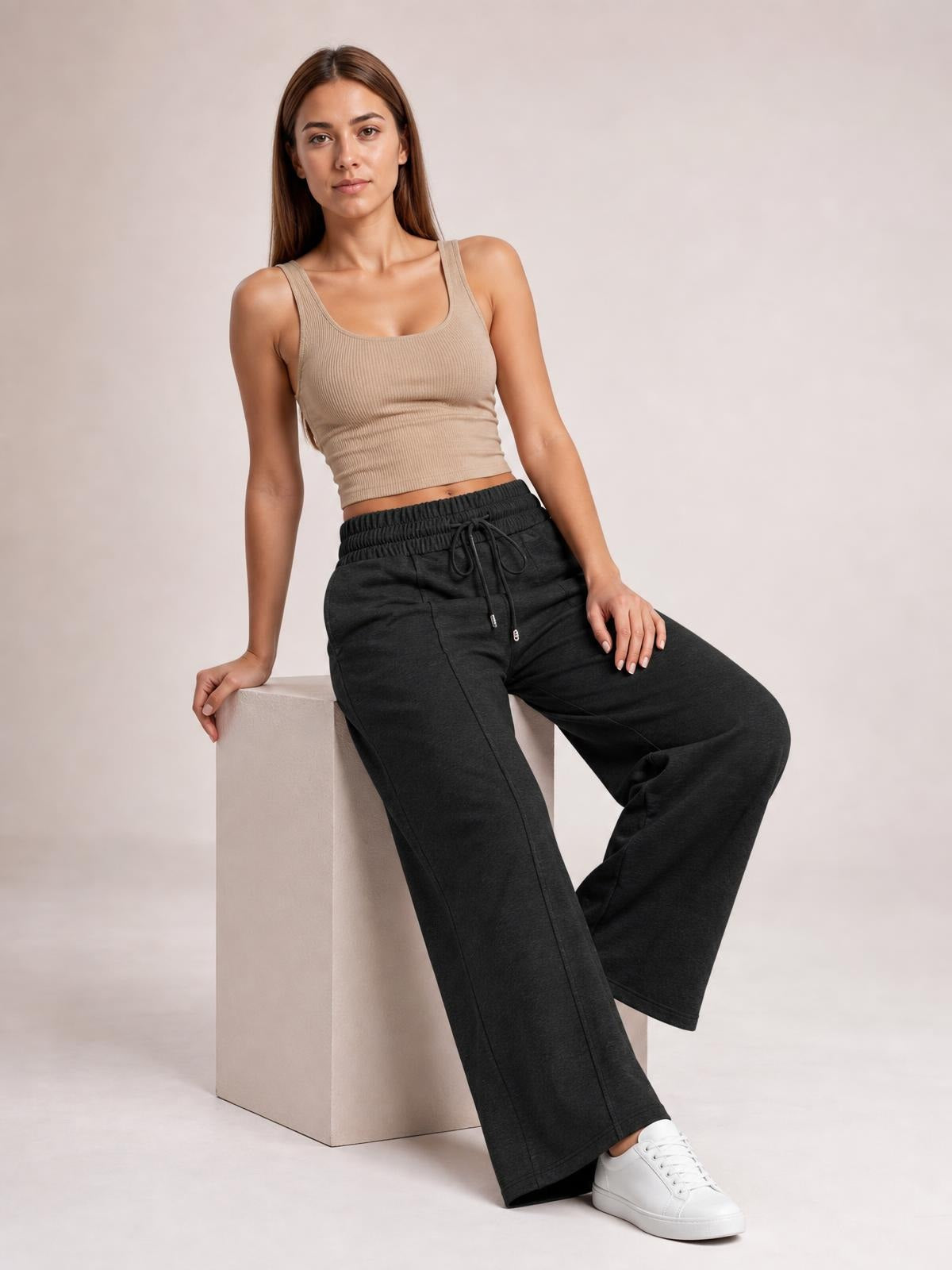 Model seated and leaning back in black drawstring elastic waist wide leg pants with a relaxed, flowy silhouette and visible front pockets.