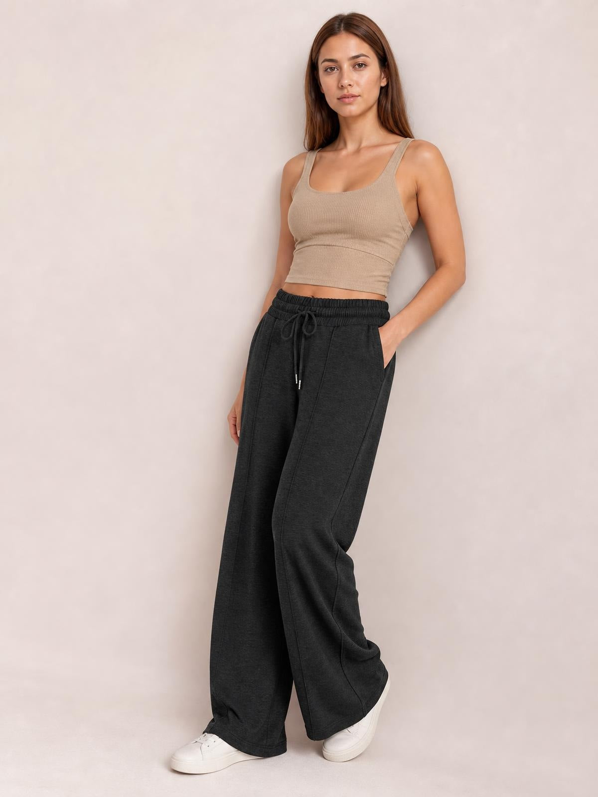 Model wearing dark charcoal drawstring elastic waist wide-leg pants with side pockets, a relaxed flowy silhouette, and hands tucked into the pockets.