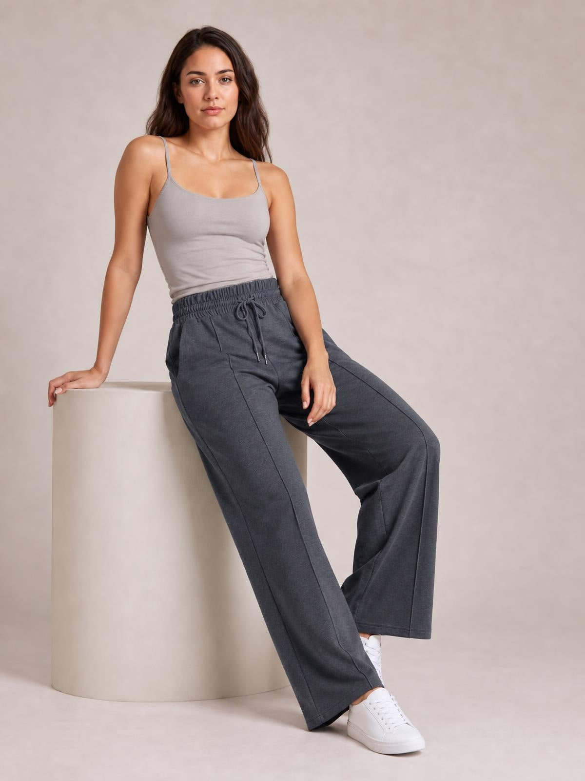 Model seated in dark gray drawstring elastic waist wide leg pants with visible pockets, relaxed flowing silhouette, and straight stitched leg construction.