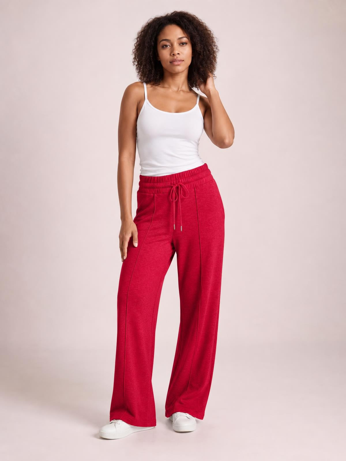 Model wearing red drawstring elastic waist wide leg pants with a relaxed silhouette, visible pockets, and long straight legs, standing with one hand raised.