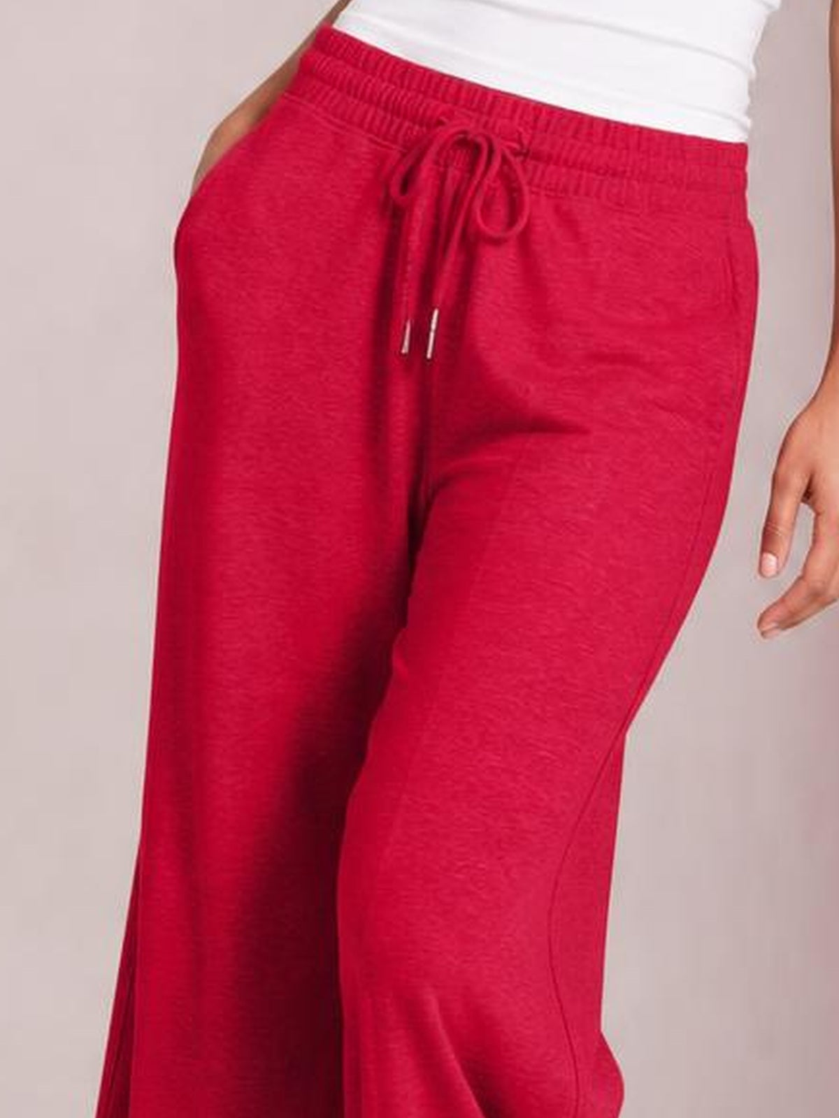 A model wears bright red drawstring elastic waist wide leg pants with a relaxed flowy silhouette, visible side pockets, and a soft textured finish.
