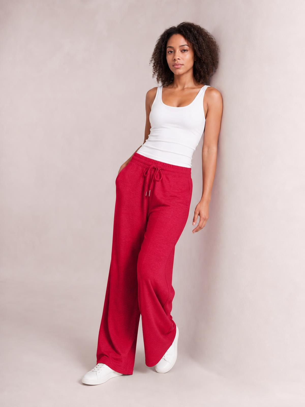 Model leans against a wall wearing red drawstring elastic waist pants with a relaxed wide-leg silhouette and visible front pockets.