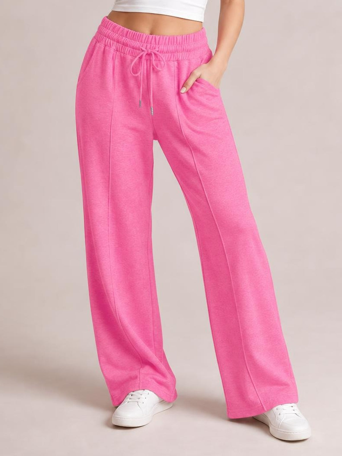 Model wearing bright pink drawstring elastic waist wide leg pants with a relaxed silhouette, front pockets, and one hand tucked into a pocket.