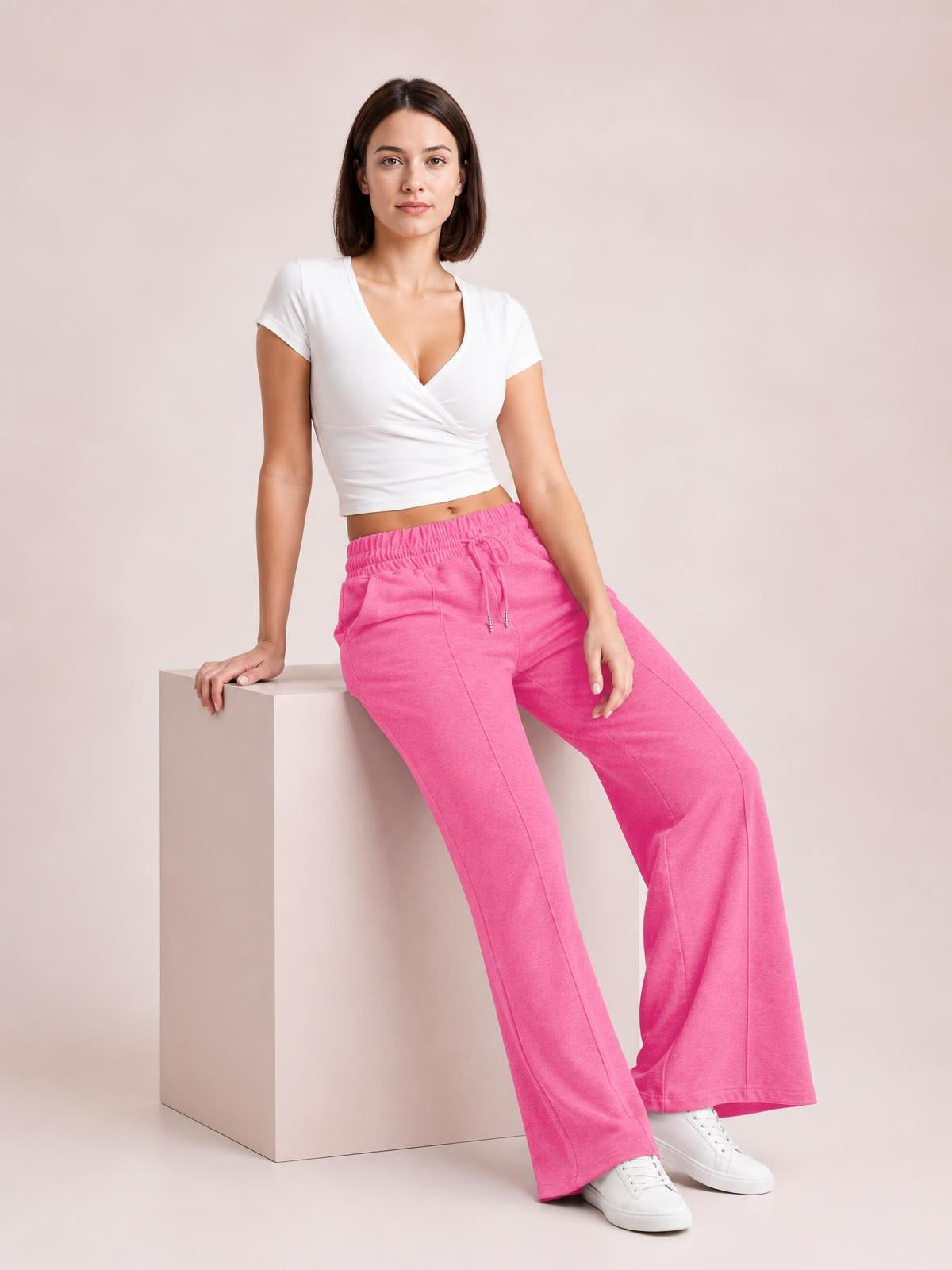 Model sits on a block wearing bright pink drawstring elastic waist wide-leg pants with front pockets and a relaxed, flowing silhouette.