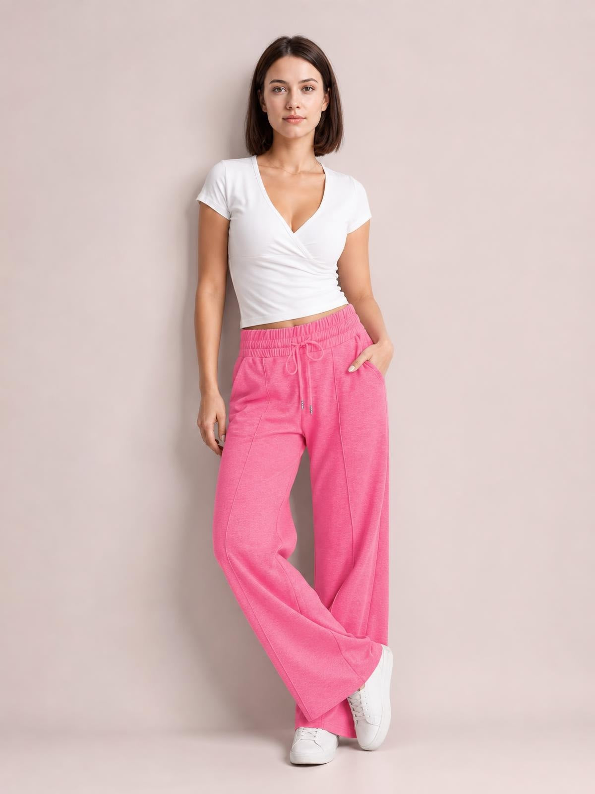 Model poses in bright pink drawstring elastic waist wide leg pants with a relaxed flowy silhouette, pocketed construction, and one hand in a pocket.