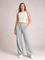 A model stands in light gray drawstring elastic waist wide leg pants with visible pockets, relaxed flowing silhouette, and a hand tucked into one pocket.
