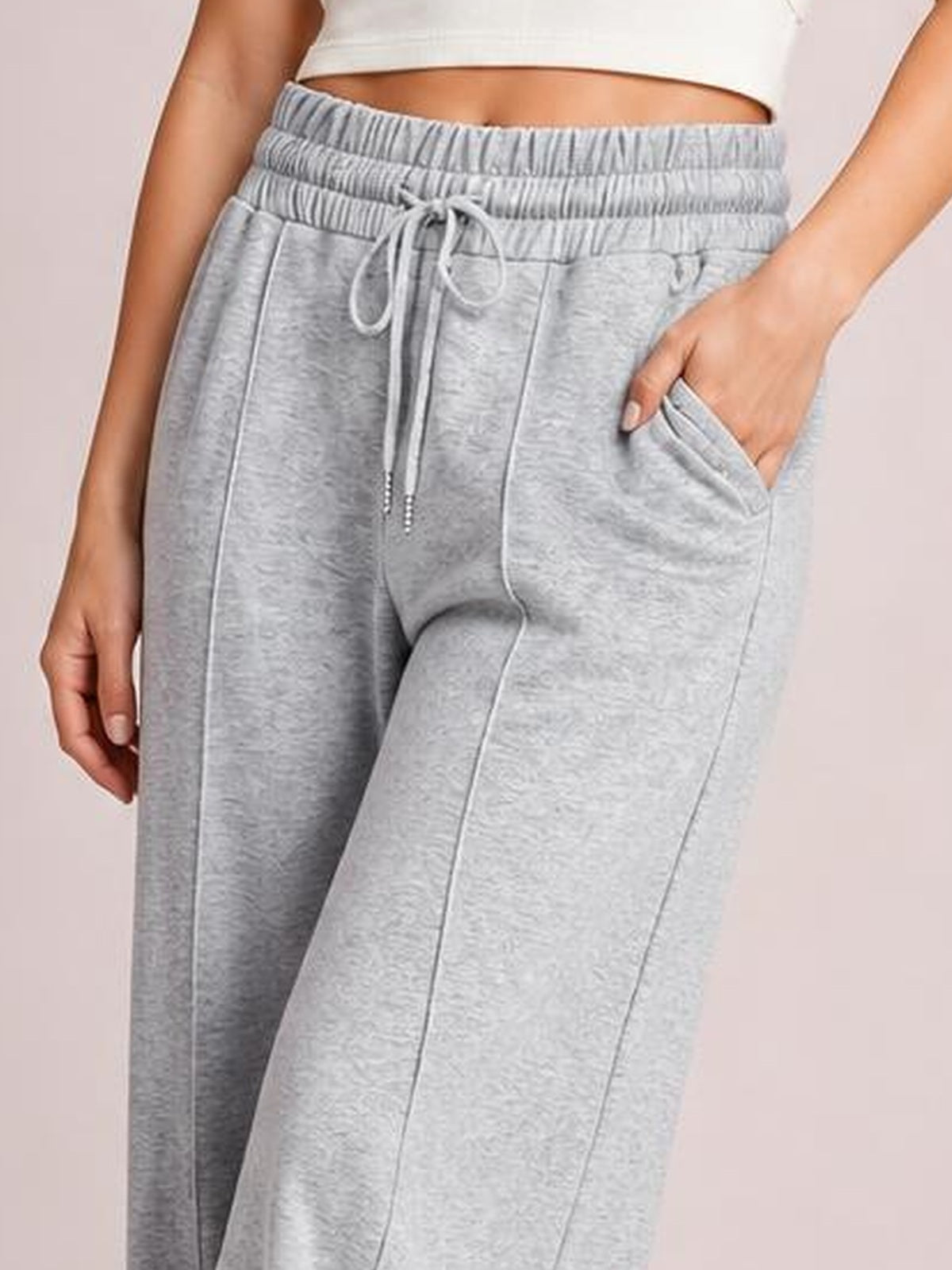Model wears light gray drawstring elastic-waist wide-leg pants with a relaxed silhouette, visible seam construction, and a hand tucked into a side pocket.