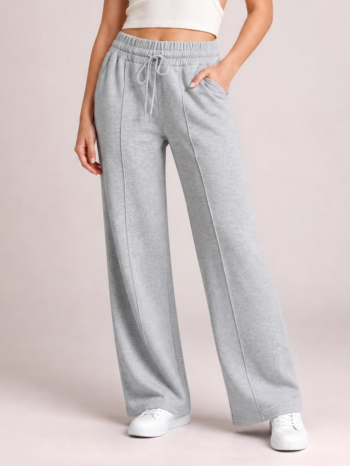 Model wearing light gray drawstring elastic waist wide leg pants with front pockets and straight seam details, standing with one hand in a pocket.
