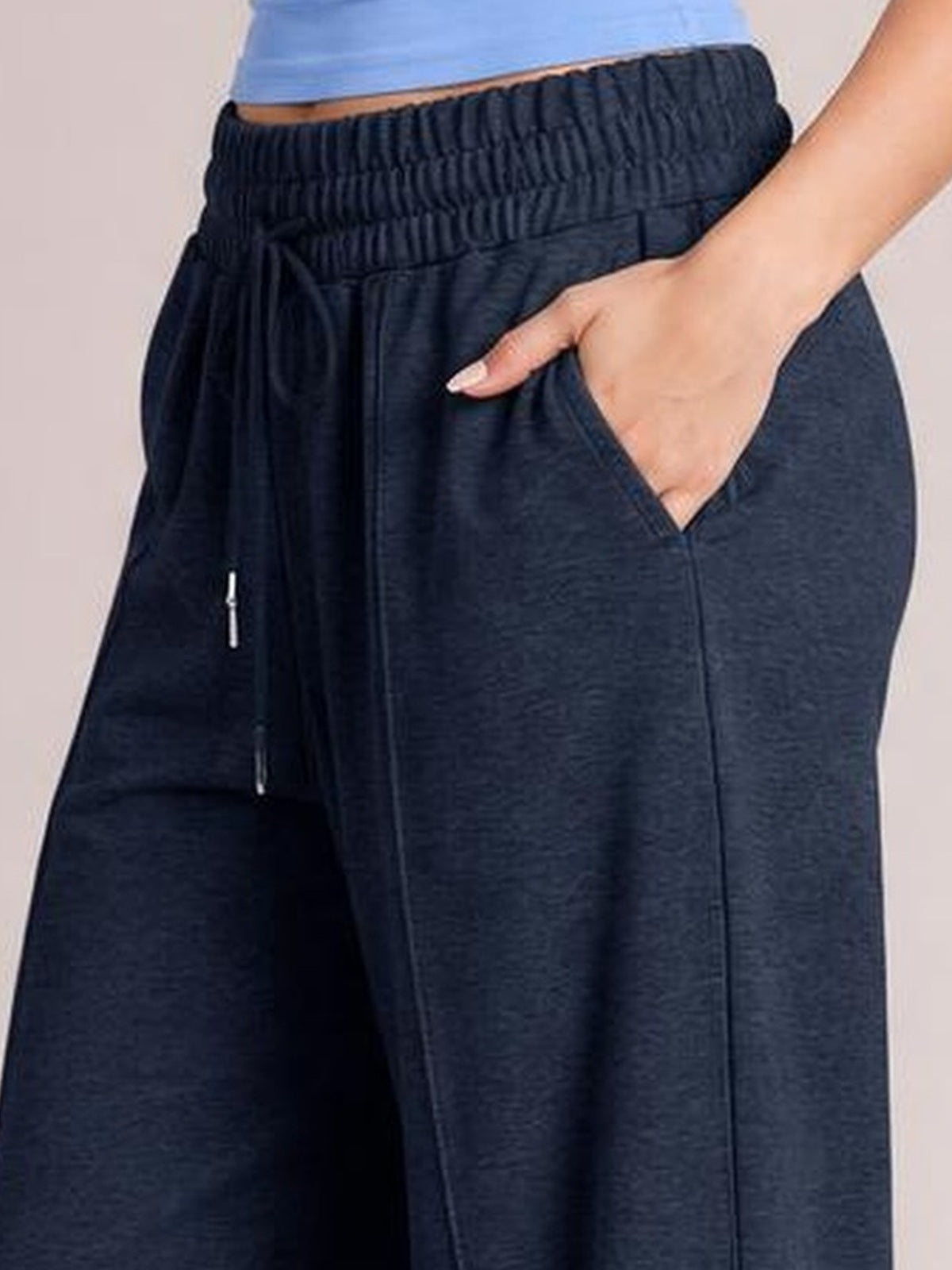 Close-up of a model wearing dark navy drawstring elastic-waist wide-leg pants, with a relaxed silhouette, visible pocket, and hand resting inside.