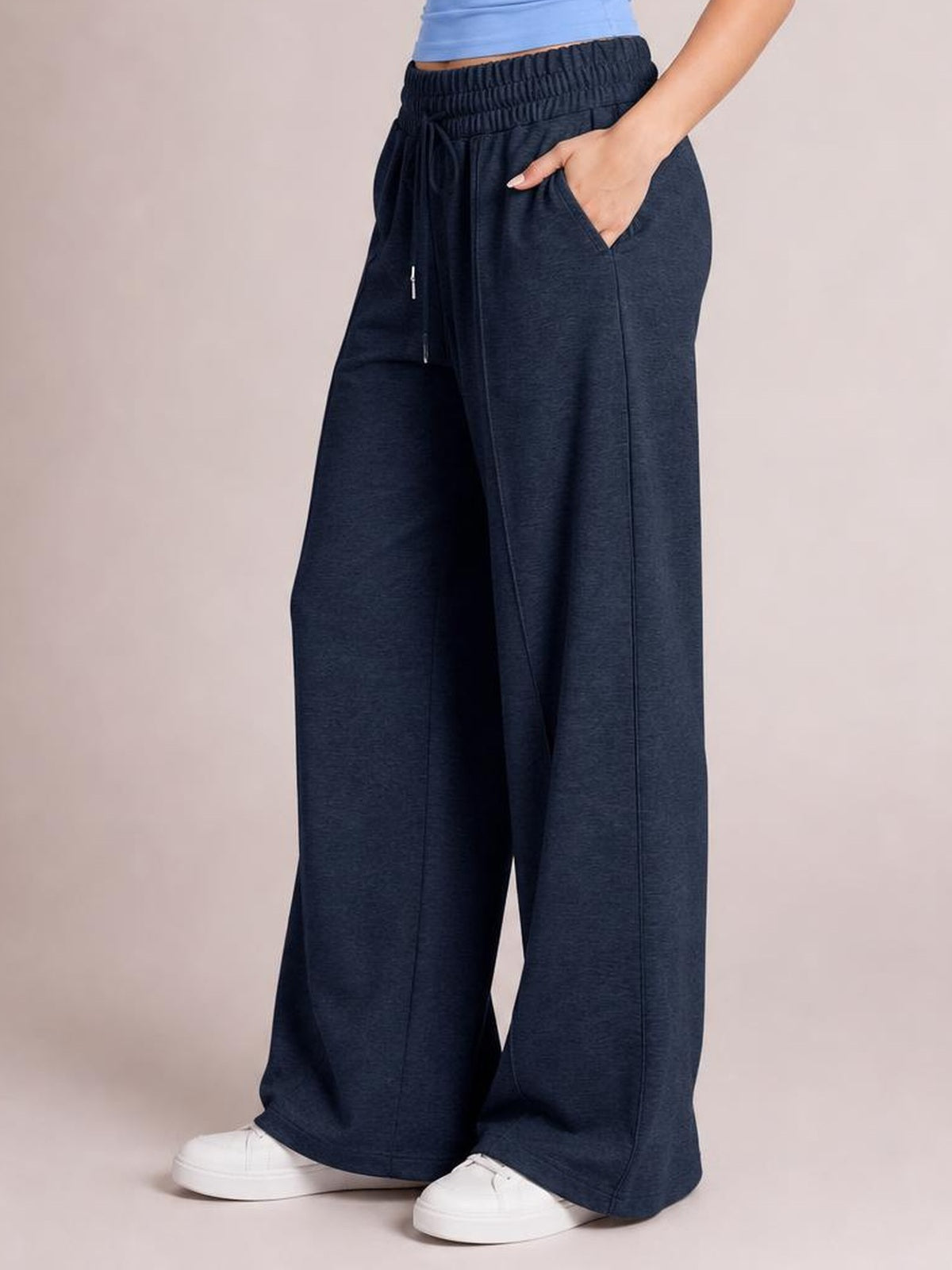 Model stands in dark navy drawstring elastic waist pants with a relaxed wide-leg silhouette, side pockets, and full-length hems over white sneakers.