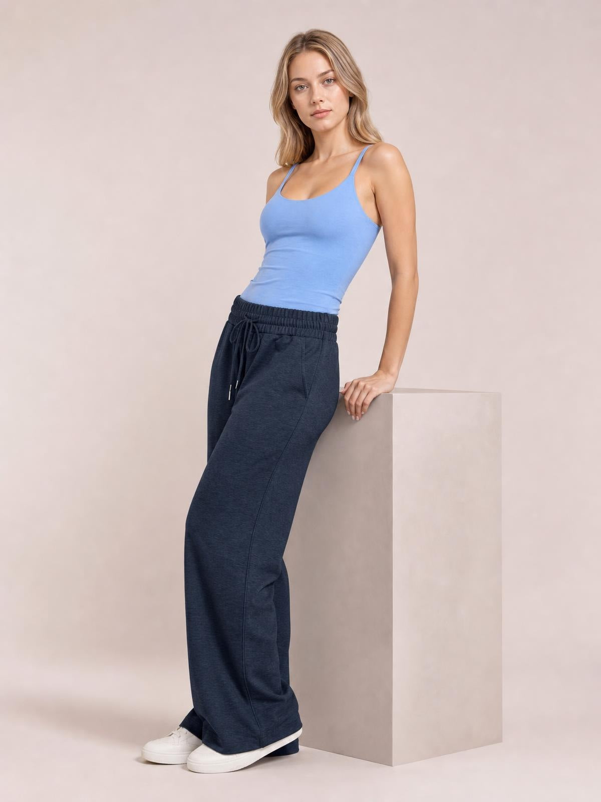 Model wearing dark navy drawstring elastic waist wide leg pants with side pockets, standing in a relaxed pose beside a block.