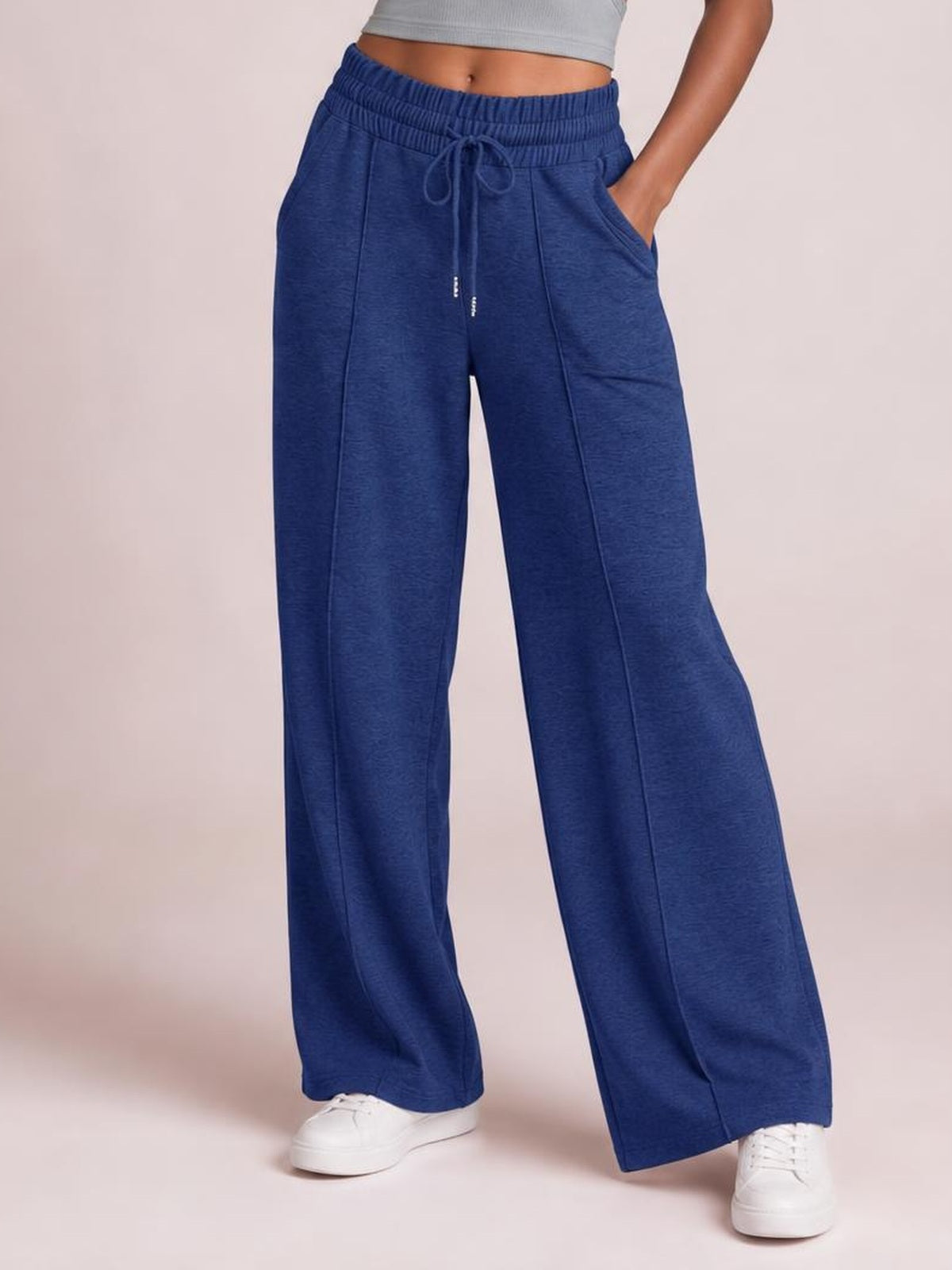 Model wearing navy blue drawstring elastic waist wide-leg pants with front pockets, relaxed flowing silhouette, and visible stitched panel construction.