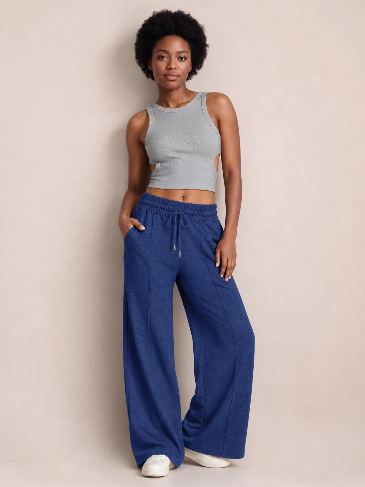 A model stands in blue drawstring elastic waist pants with a relaxed wide-leg silhouette, visible side pockets, and one hand tucked into a pocket.