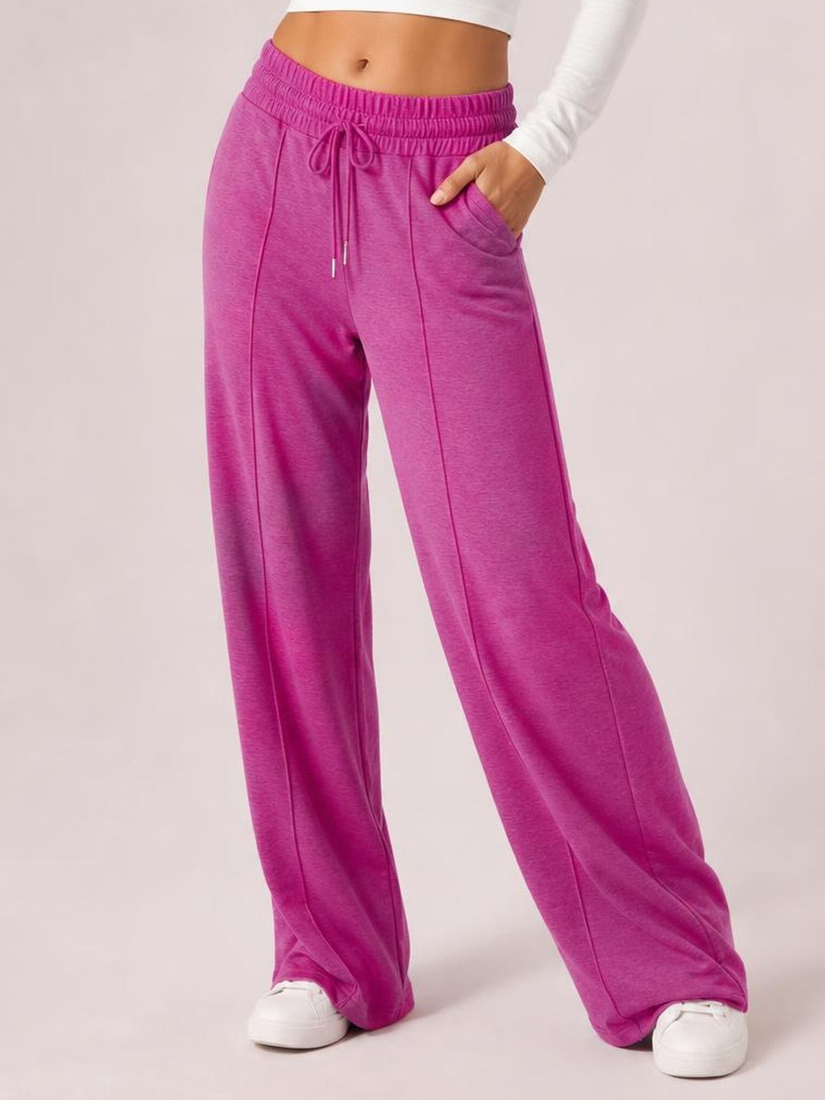 A model poses in magenta drawstring elastic waist pants with wide legs, visible front seam details, and a side pocket with one hand tucked inside.