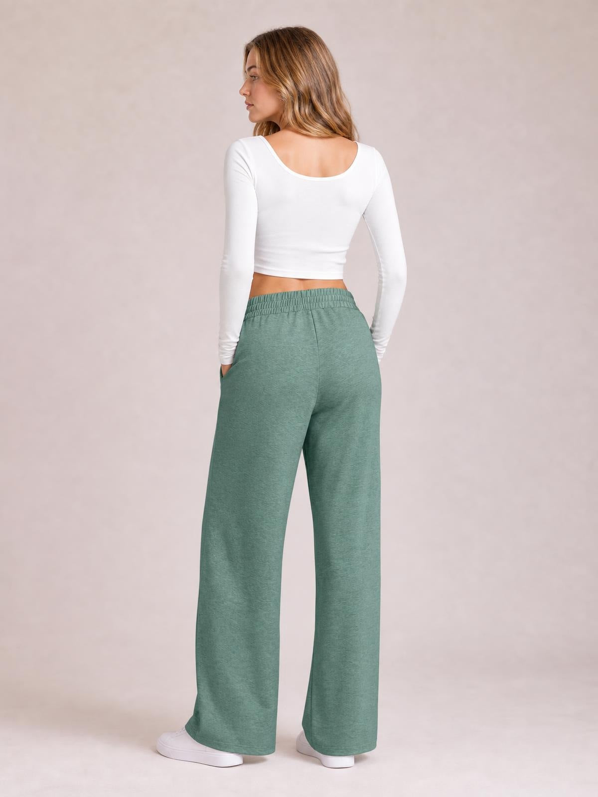 Model turned slightly away wears sage green drawstring elastic-waist wide-leg pants with roomy pocketed construction and a flowing silhouette.