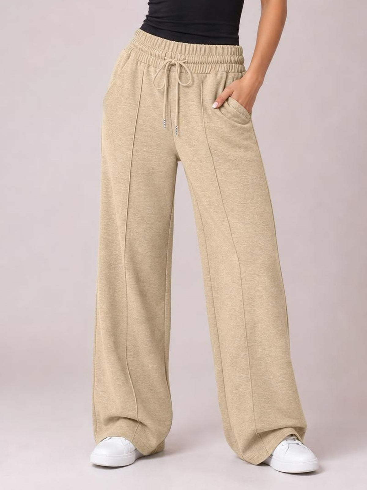 Model wears beige drawstring elastic waist wide leg pants with oversized pockets, long flowing legs, and visible front seam detailing.