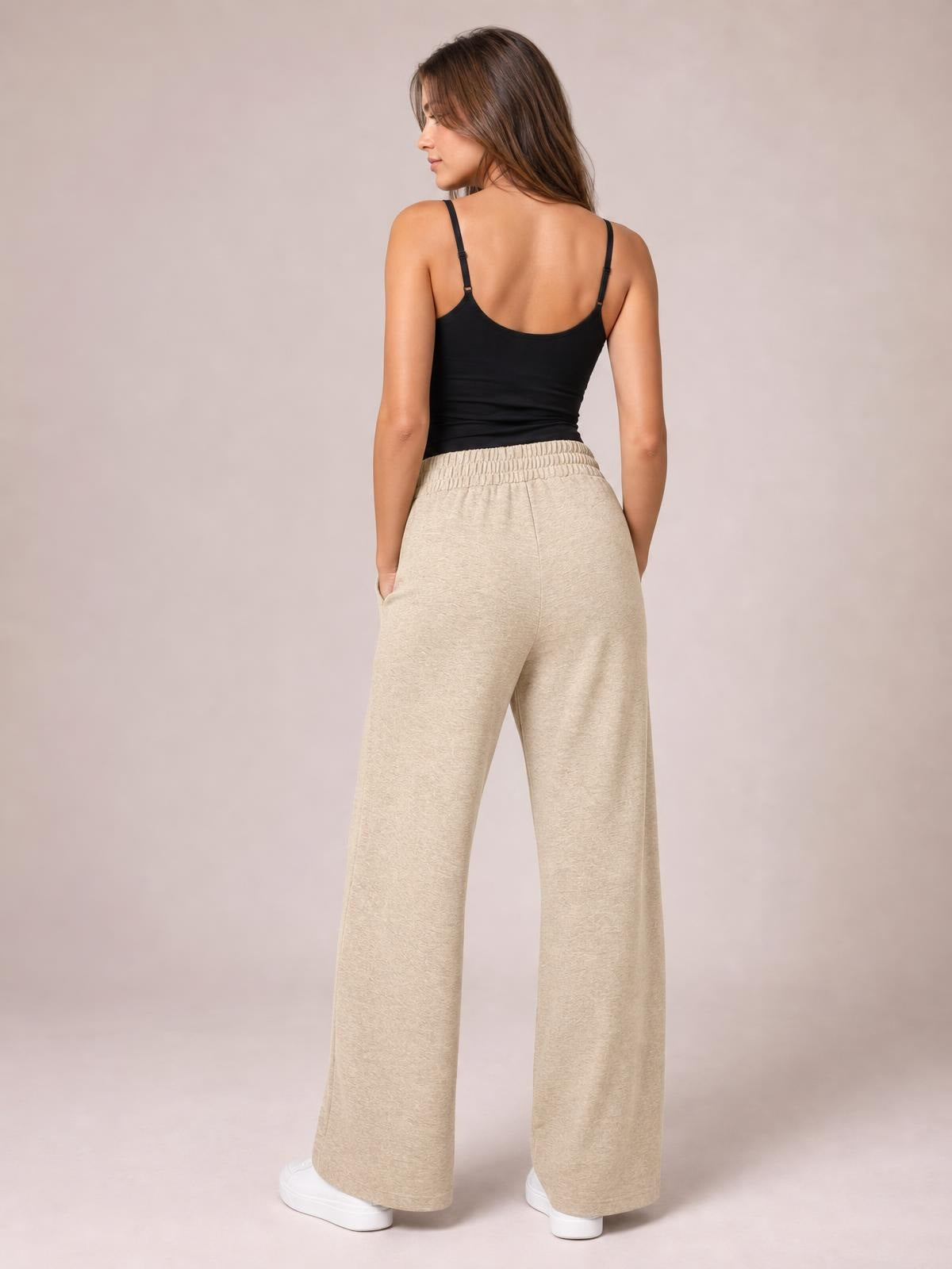 Model shown from behind wearing beige drawstring elastic-waist wide-leg pants with a relaxed, flowing silhouette and side pockets.
