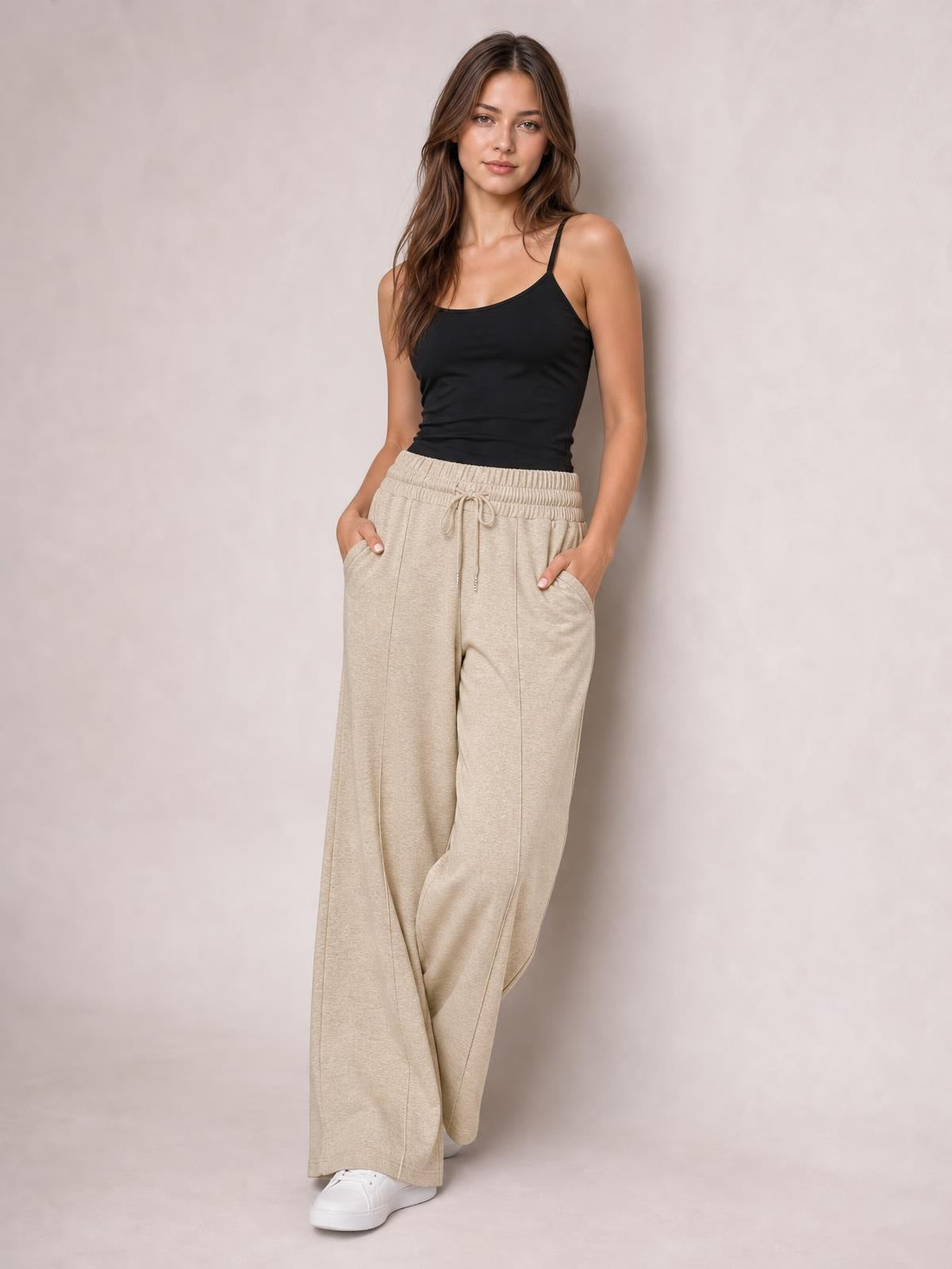 Model poses in beige drawstring elastic-waist wide-leg pants with front pockets, flowing relaxed silhouette, and crossed ankles.