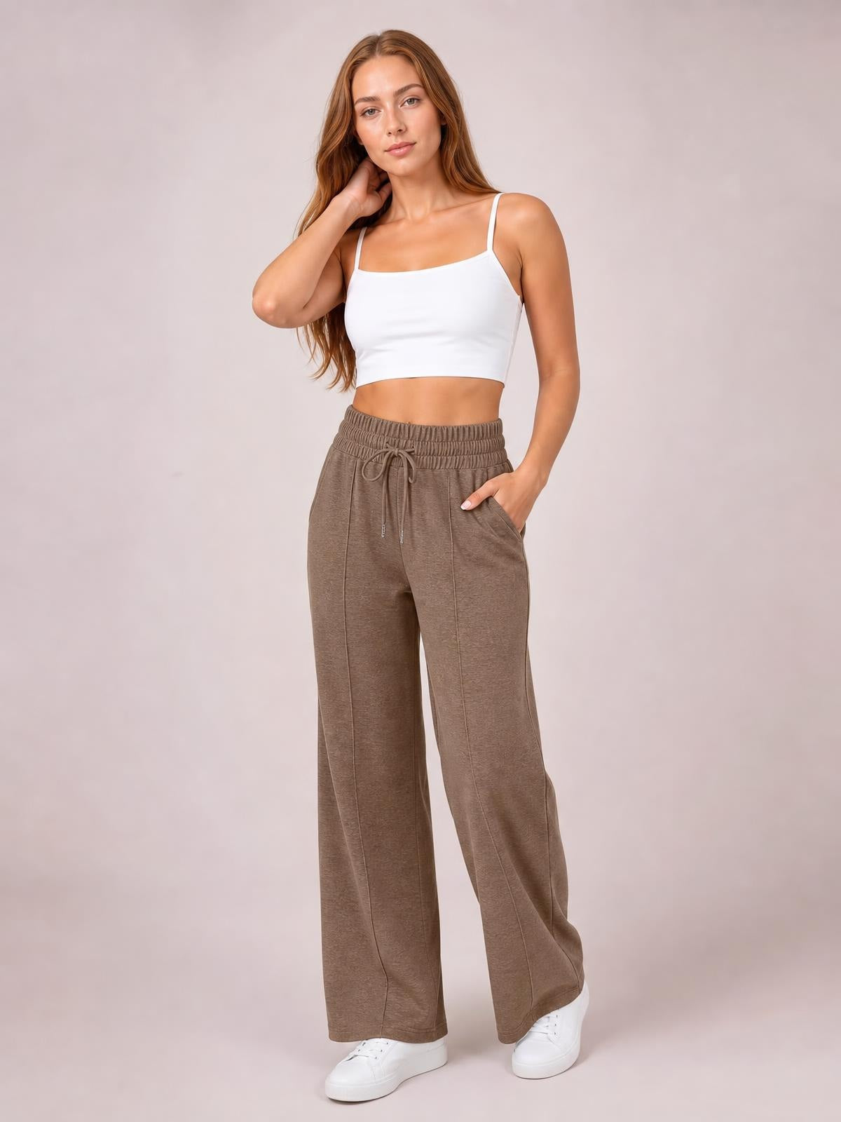Model wearing taupe drawstring elastic waist wide-leg pants with side pockets, relaxed flowy silhouette, and visible vertical seam construction.