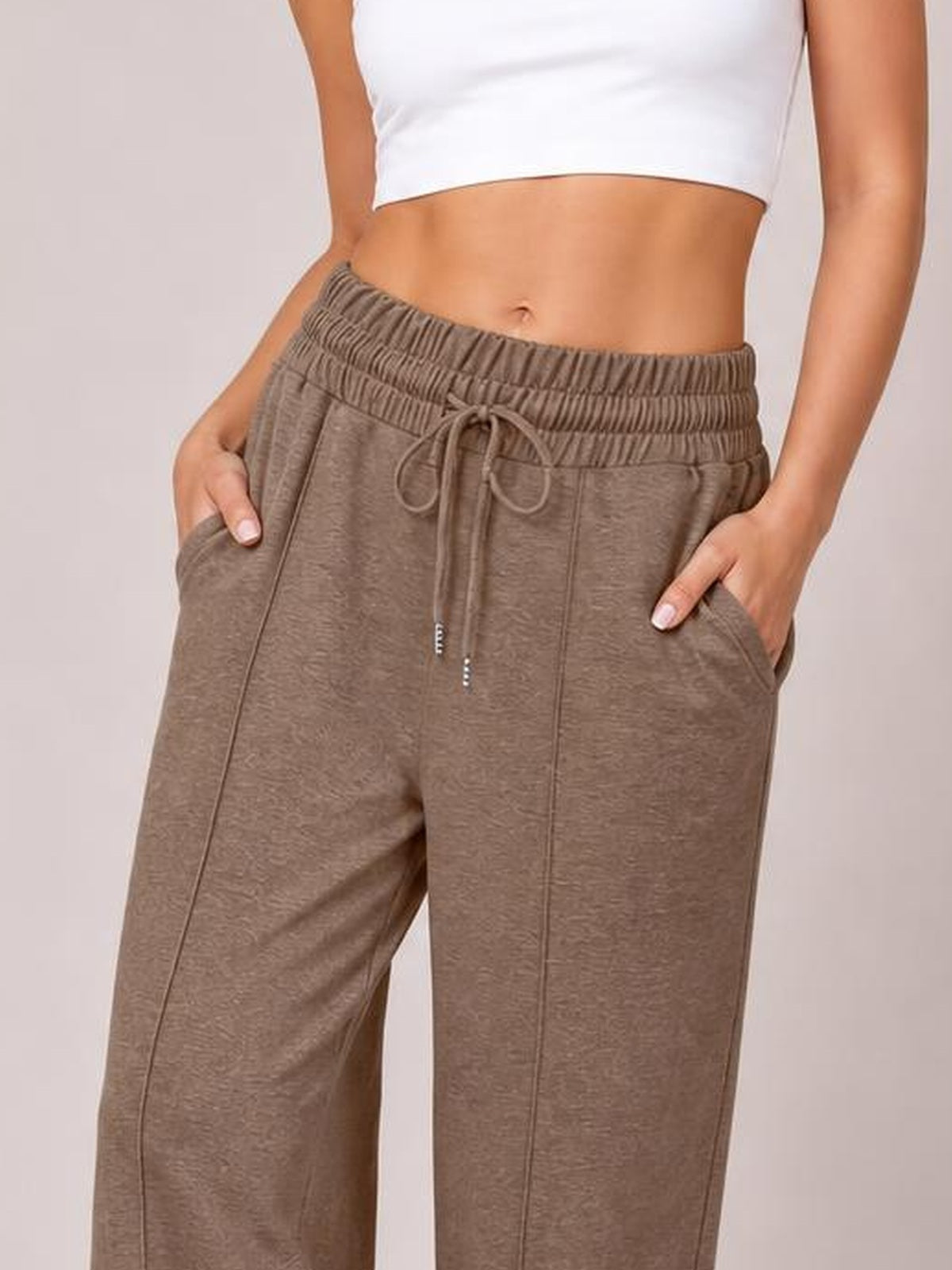 Model wearing taupe drawstring elastic waist wide-leg pants with front pockets, visible seam details, and hands resting in the pockets.