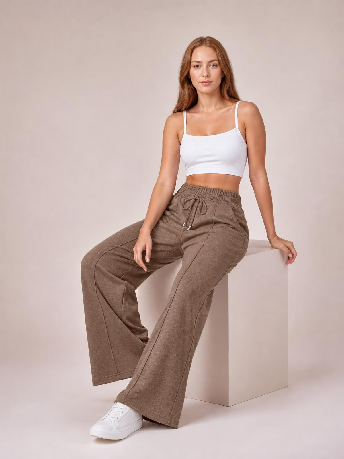Model seated and wearing taupe drawstring elastic-waist wide-leg pants with a relaxed silhouette, visible pockets, and straight seam detailing.