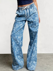Model wearing light blue washed floral wide-leg jeans with a drawstring elastic waist, front pockets, and relaxed full-length silhouette.