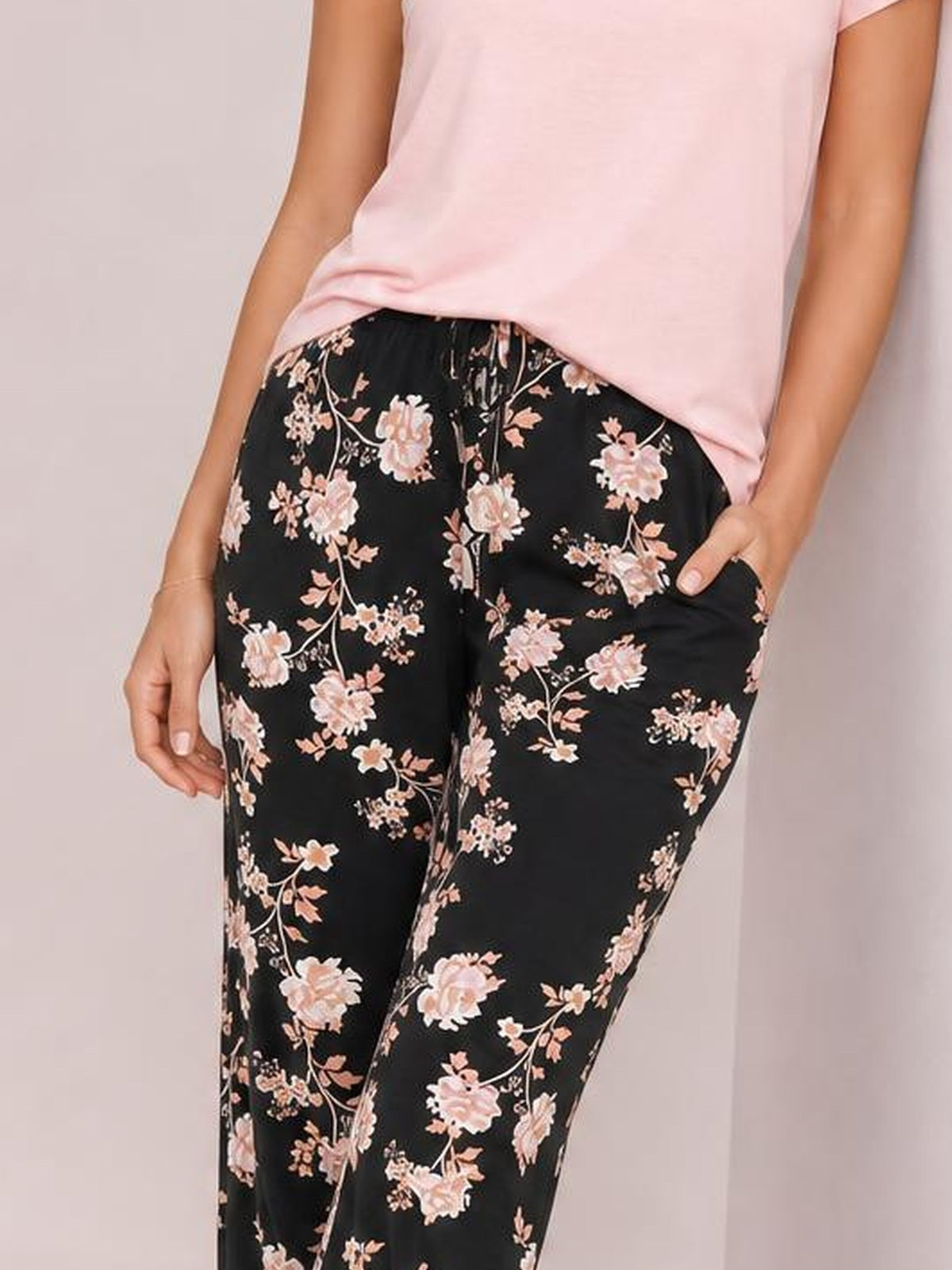 Model poses with one hand in the pocket of black drawstring flower pants featuring a relaxed straight-leg silhouette and pink floral print.