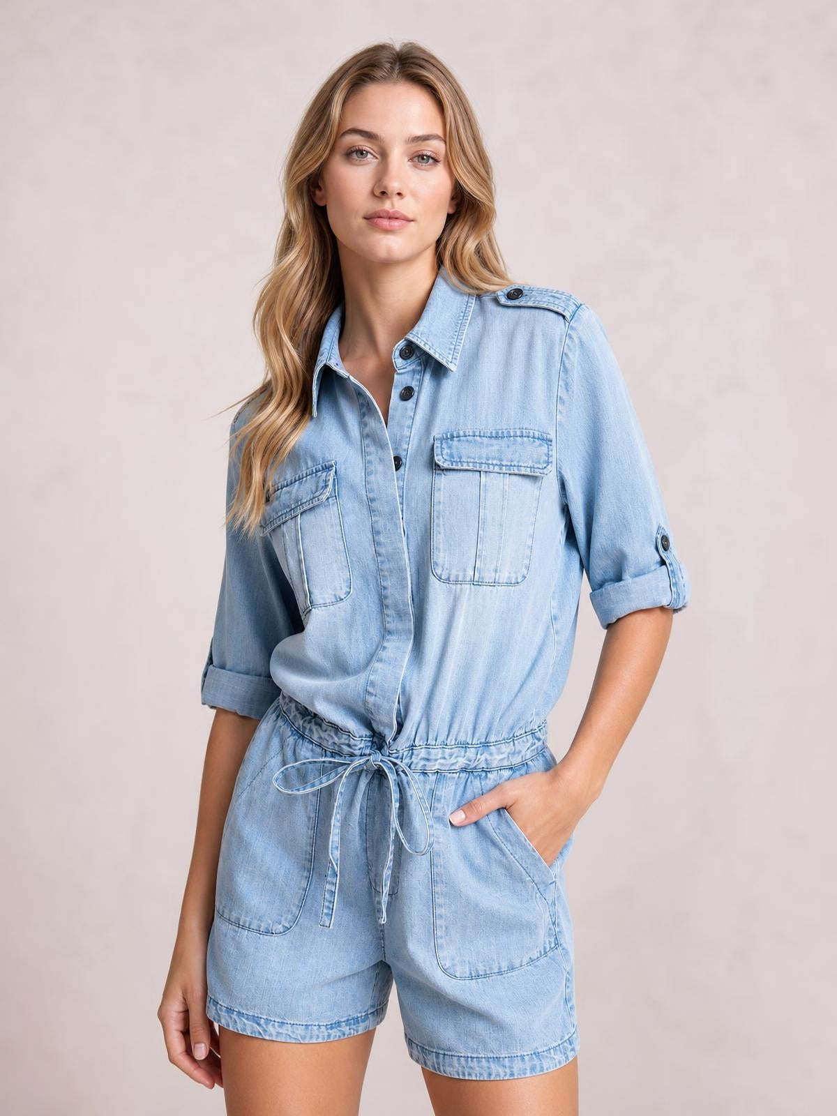 Model wears a light blue denim romper with a half-button front, rolled half sleeves, drawstring waist, utility pockets, and relaxed shorts.